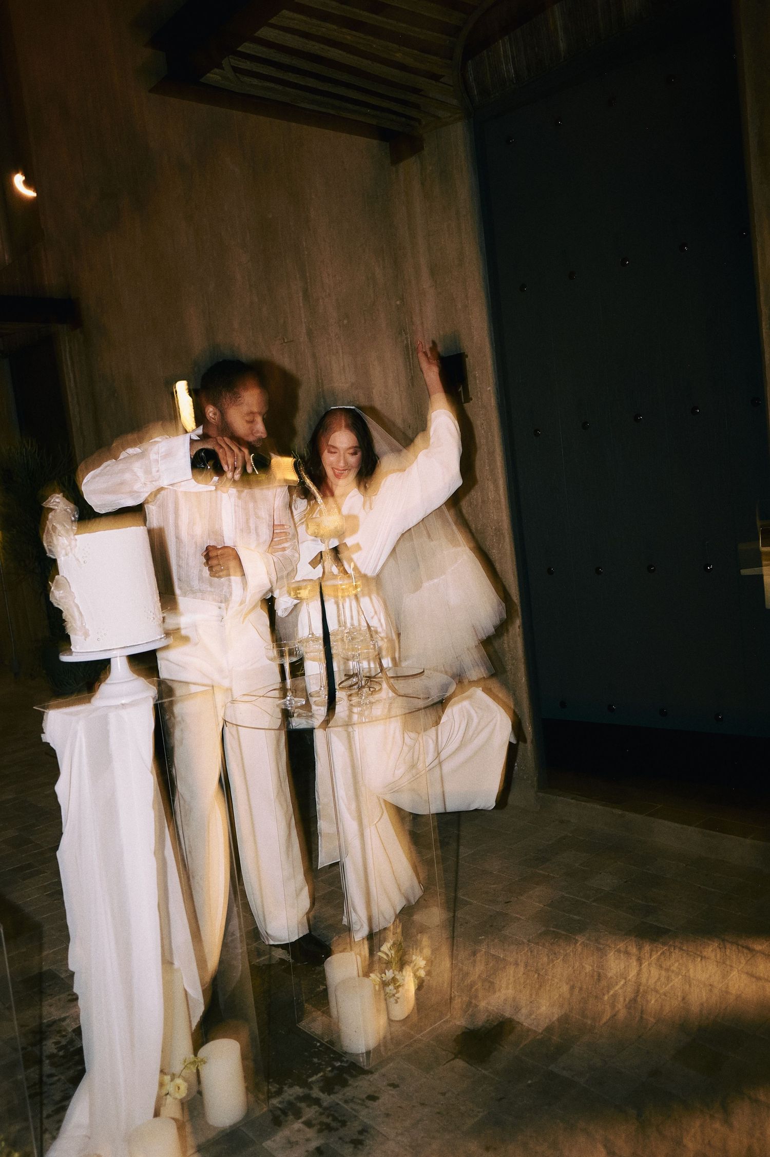 Wedding party in all-white attire poses in a dark atmospheric hallway.