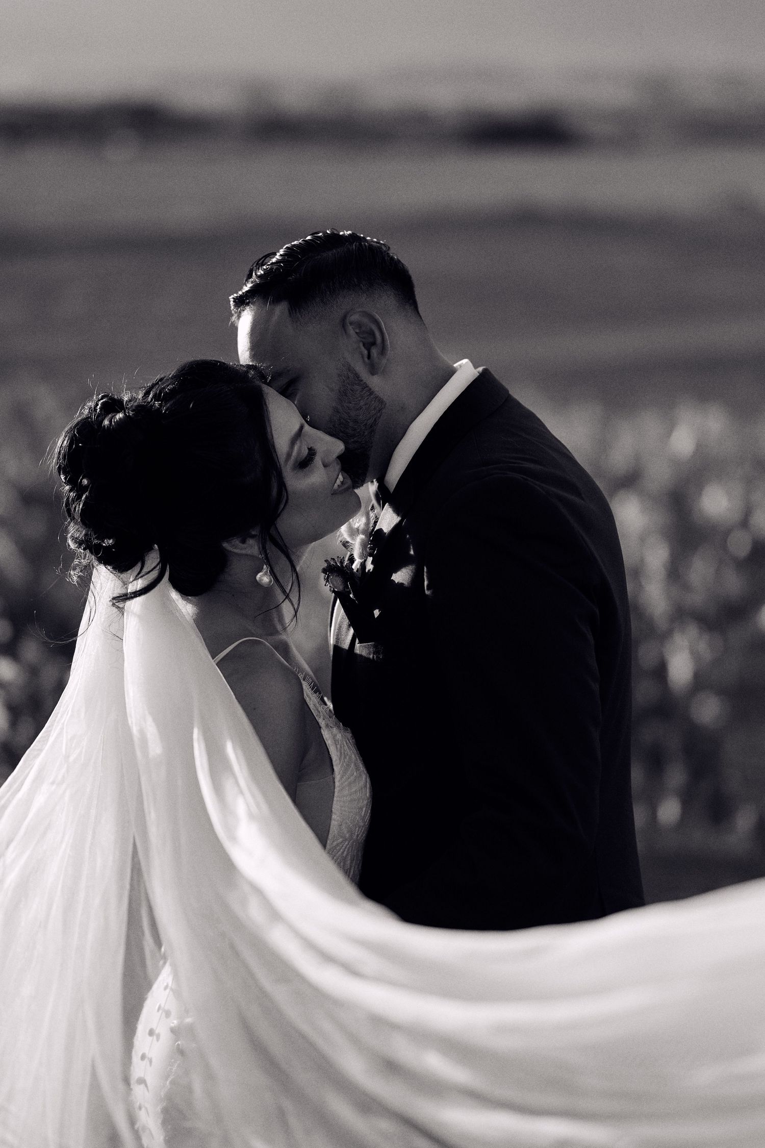 A romantic black and white wedding portrait showing a couple kissing with the bride's long veil flowing in the breeze.