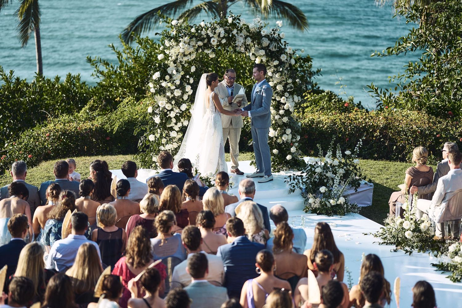 Oceanfront wedding ceremony setup with guests seated facing the tropical beach view.