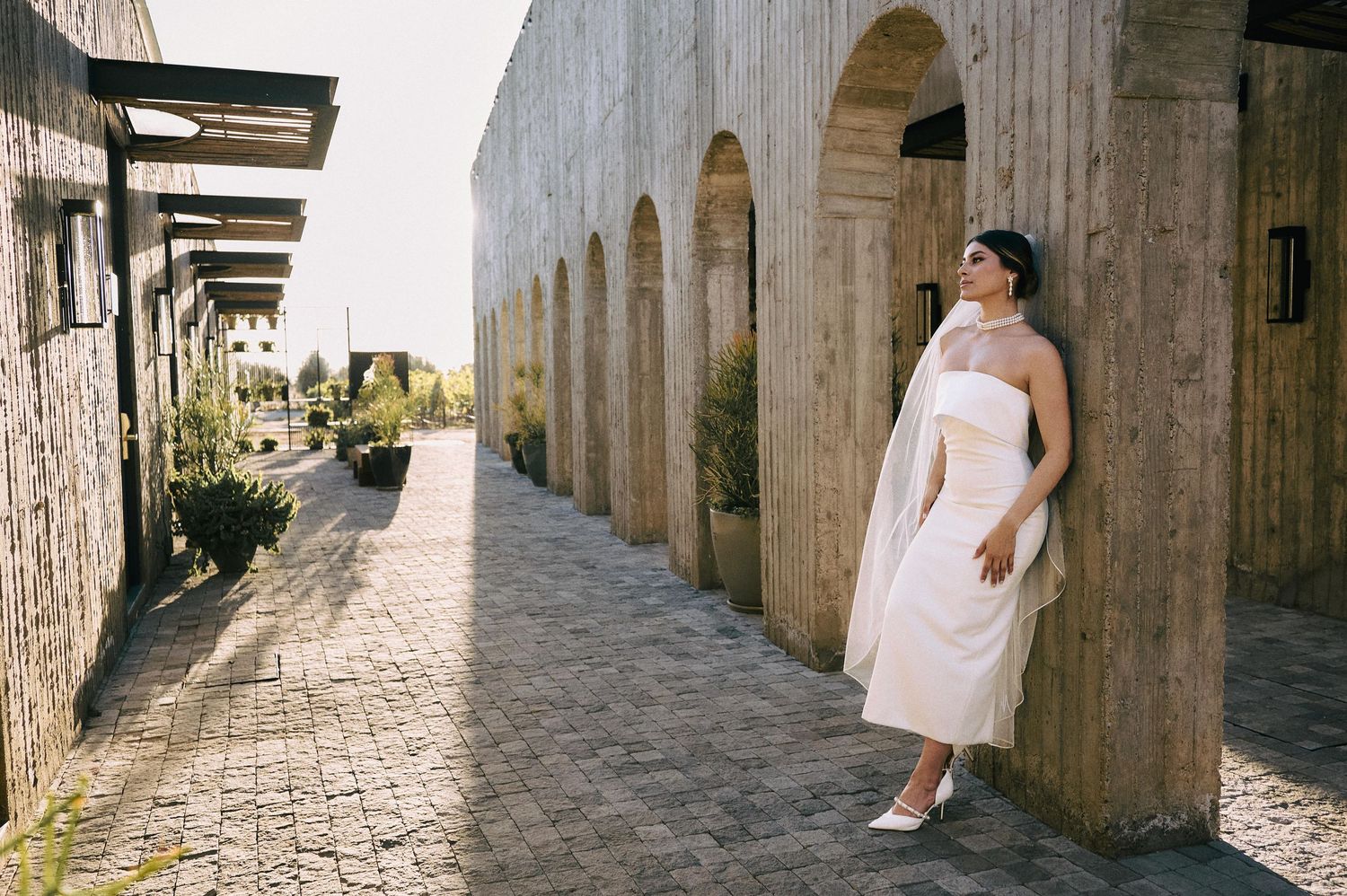 Maternity portrait of woman in white dress leaning against stone archway in historic setting.