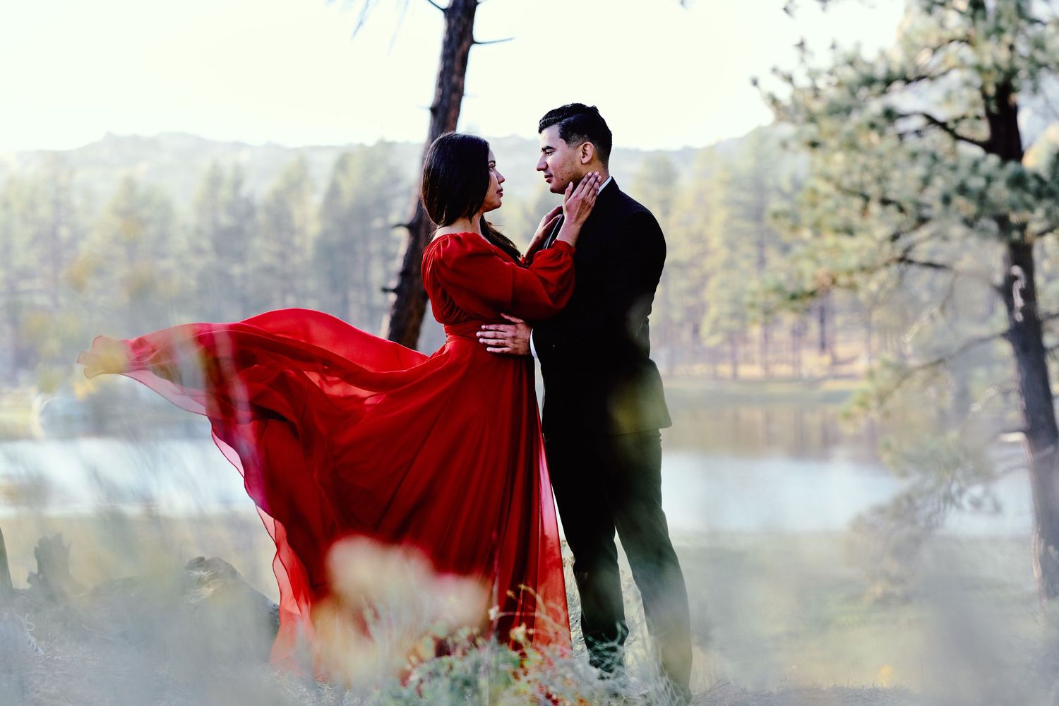 Dramatic engagement photos with flowing red fabric in misty forest setting.