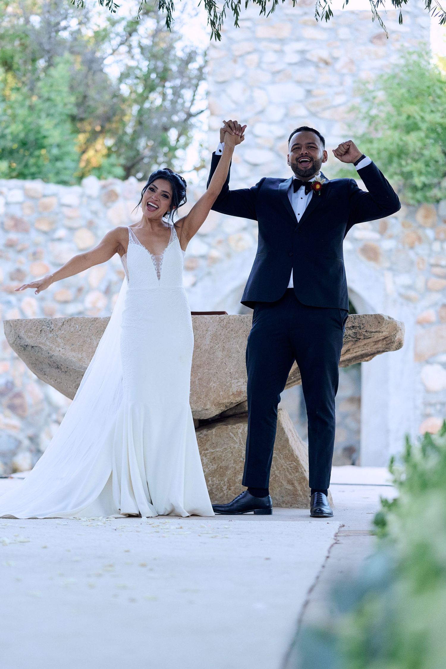 Wedding couple celebrates joyfully on stone steps in formal attire.