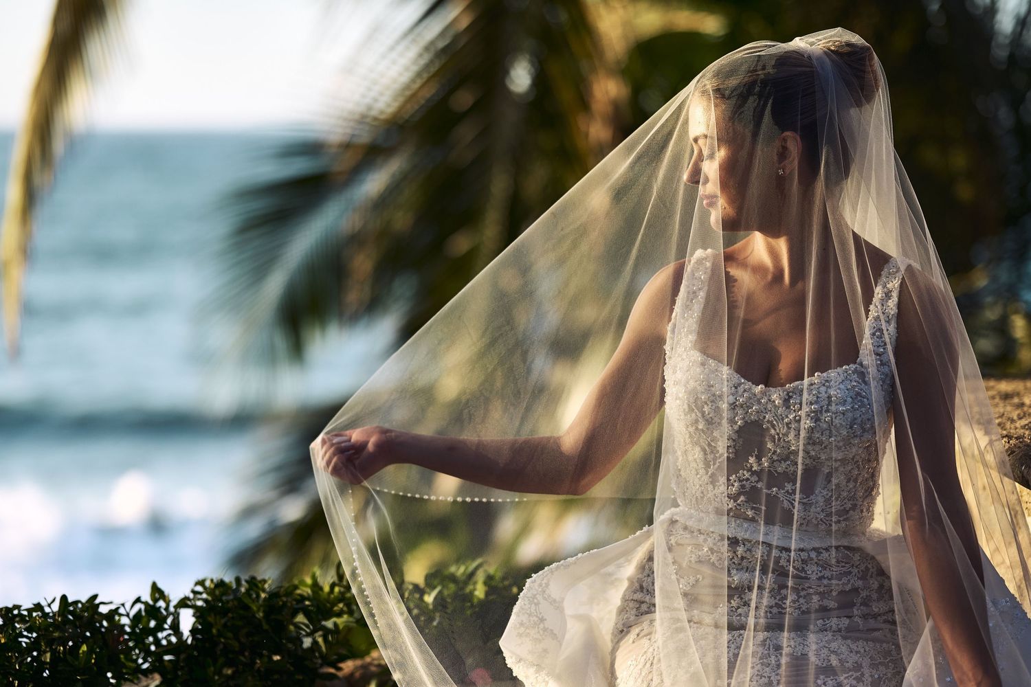 Wedding veil flowing in the ocean breeze with palm trees and beach in background.