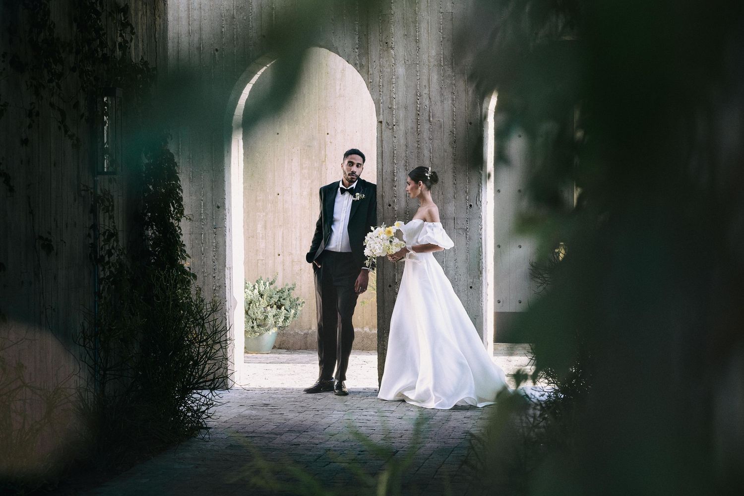 Elegant wedding portrait in a stone archway with dramatic lighting.