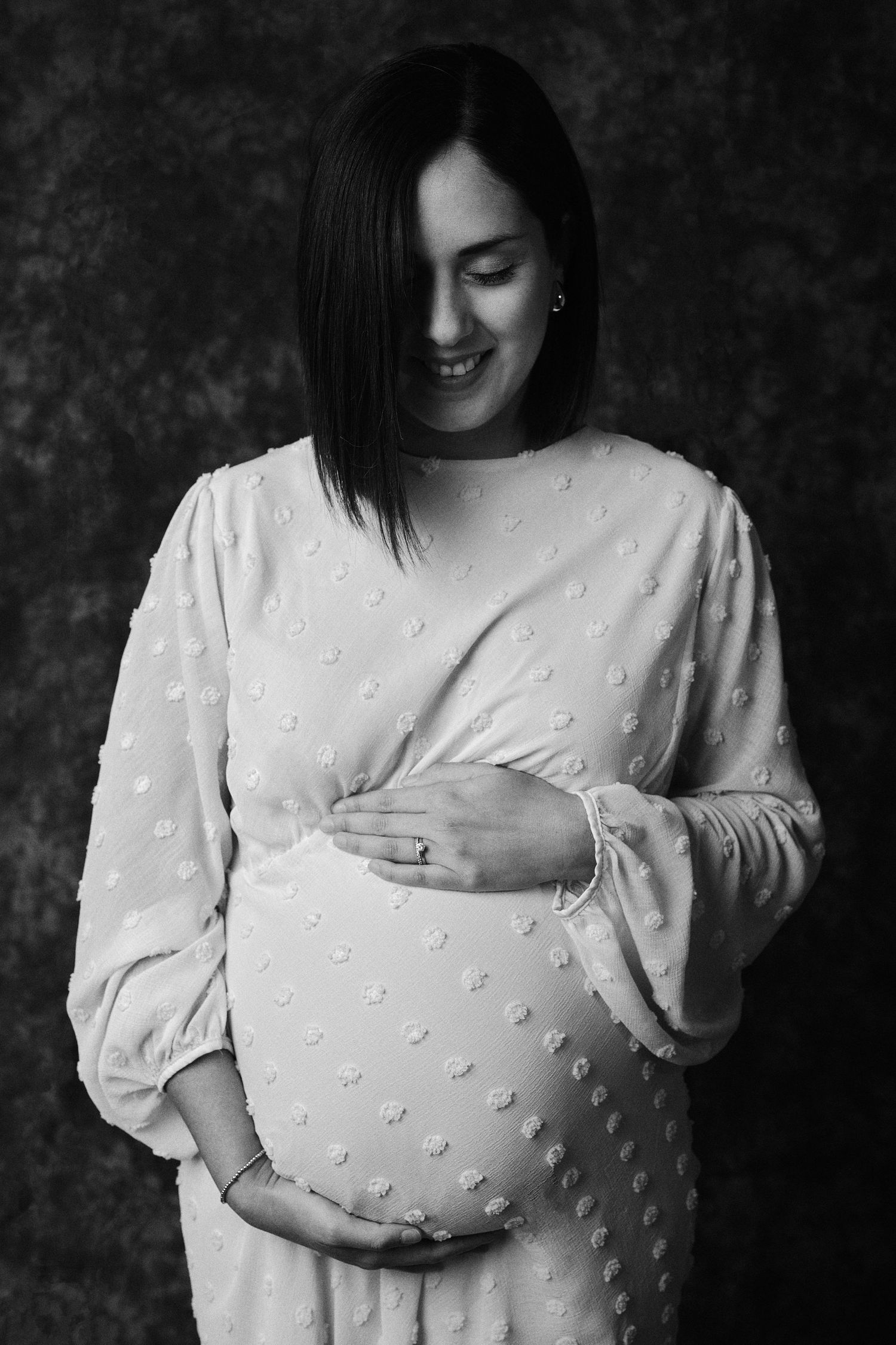 Intimate black and white maternity portrait showing gentle moment with hands on belly.