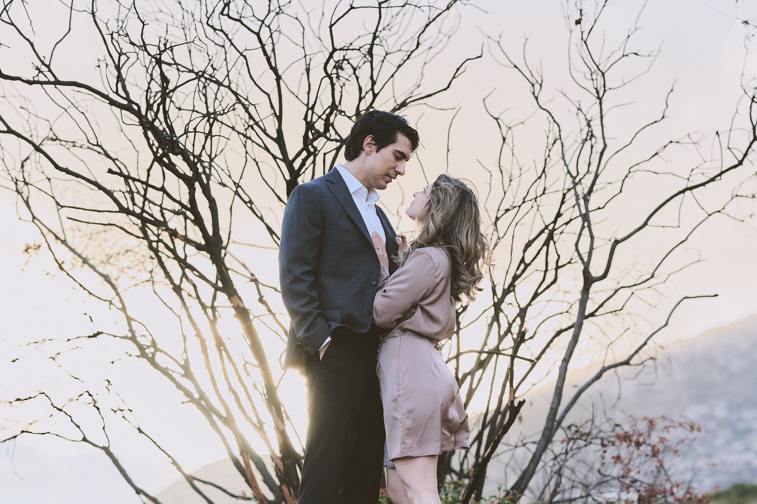 Romantic couple poses among bare winter branches at sunset.