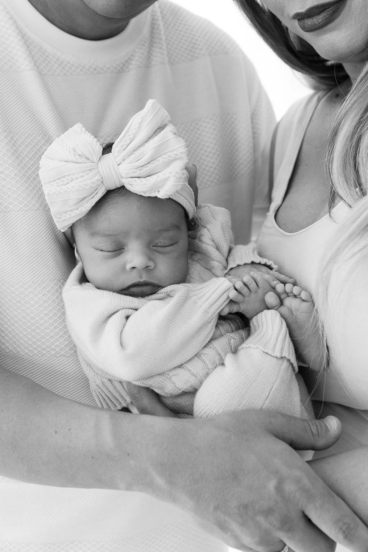 Black and white photo series showing a sleeping newborn baby wearing a white bow headband in various tender poses.