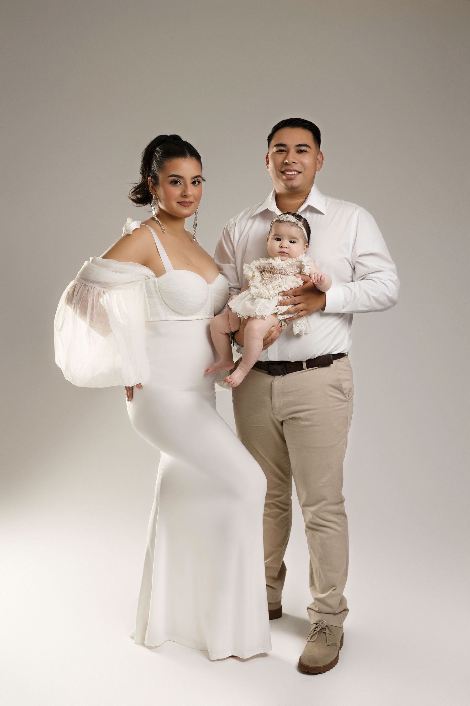 Family maternity photoshoot with couple in white and beige outfits against neutral backdrop.  Located in Palm Desert, California.