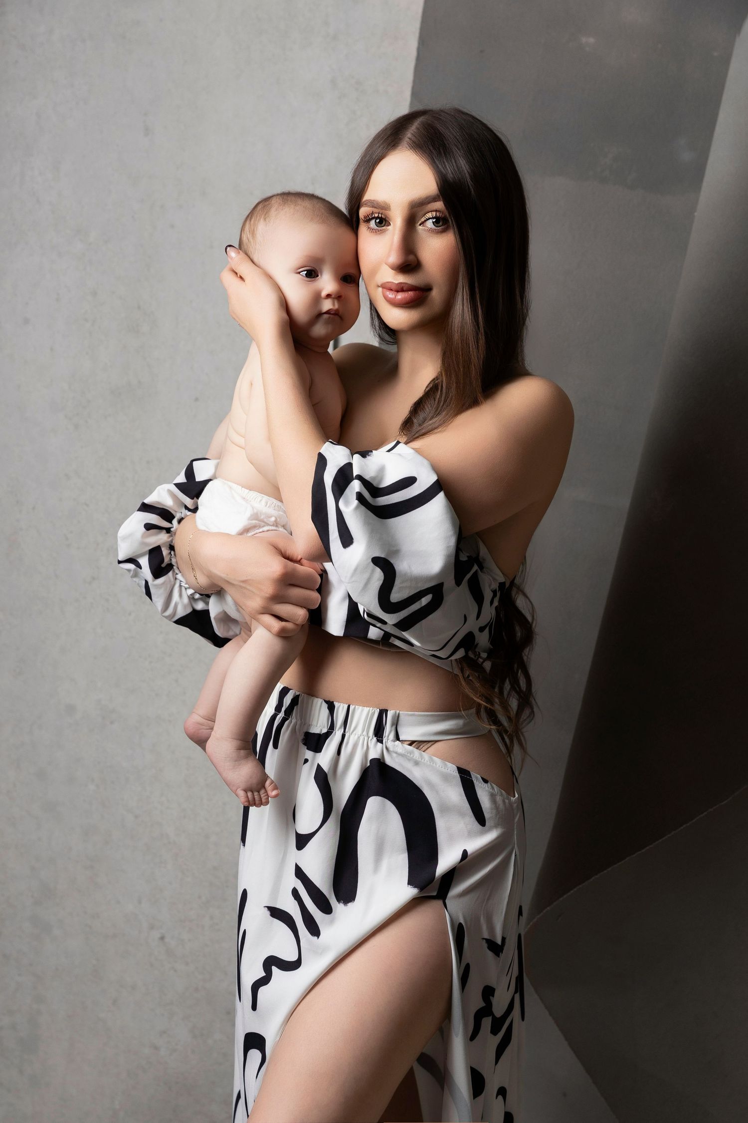 Mother and baby wearing matching black and white abstract print outfits pose together in studio setting.