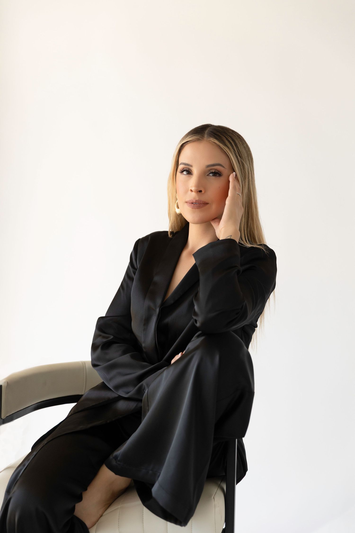 A professional portrait of a woman in black business attire seated elegantly in a white chair.