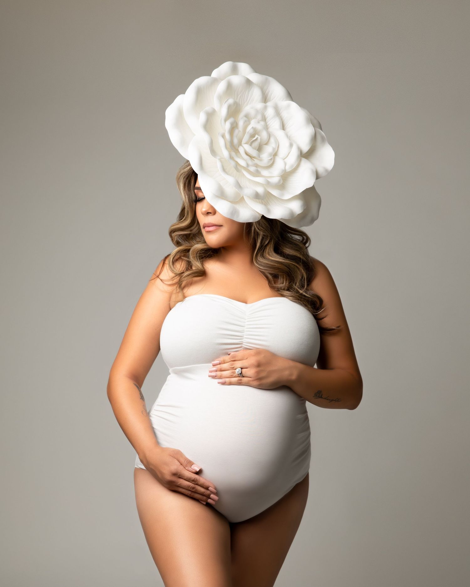 A maternity photoshoot series showing a pregnant woman in white against a grey background holding her belly.