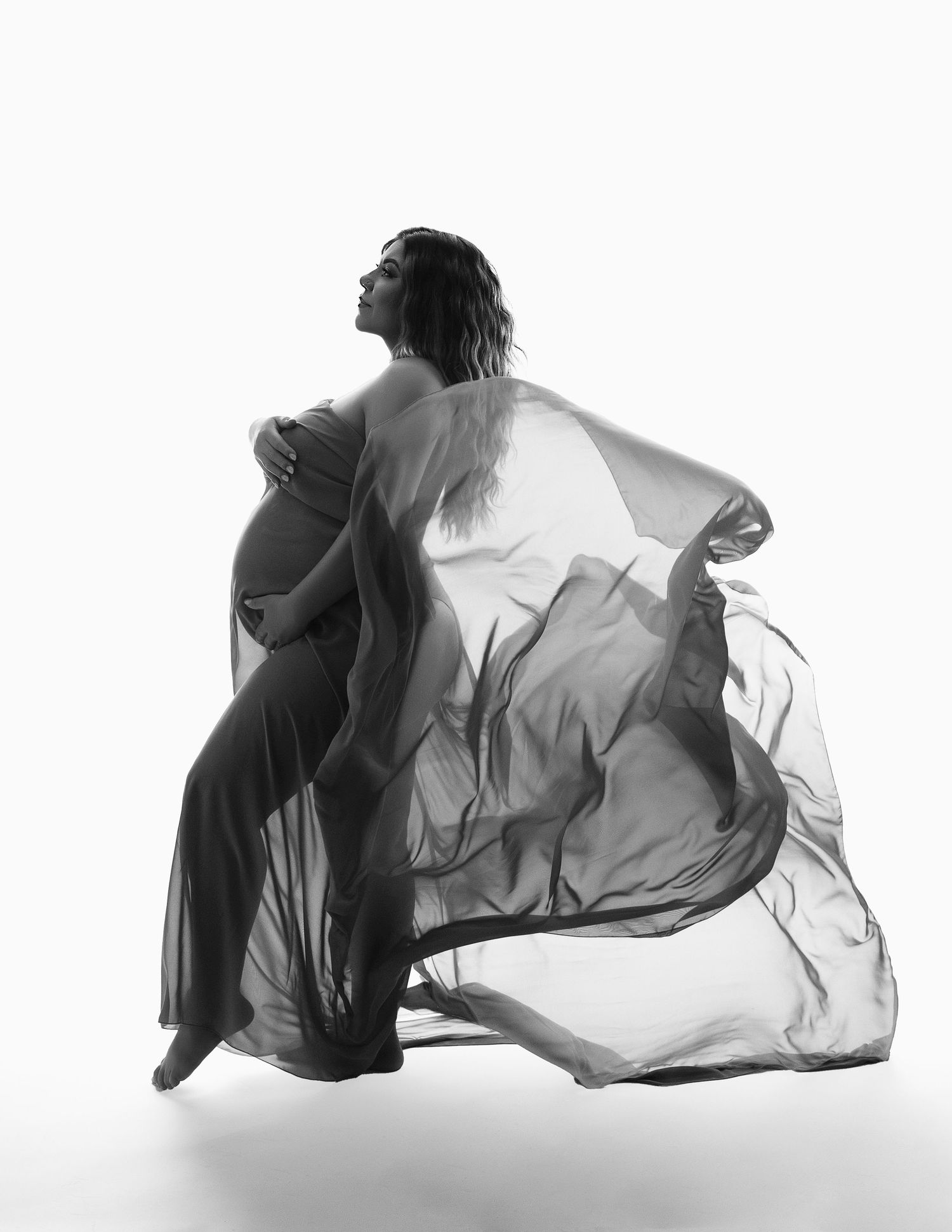 Black and white artistic photograph of a dancer in flowing fabric creating dramatic movement and silhouette.