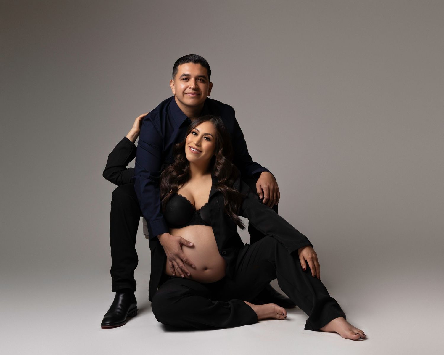 Professional maternity photoshoot with couple in dark clothing against light background.  Located in Palm Desert, California.