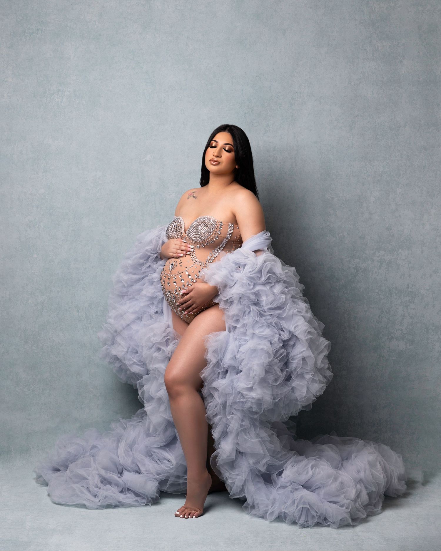 A maternity photoshoot featuring a flowing gray tulle gown against a textured gray backdrop in multiple artistic poses.