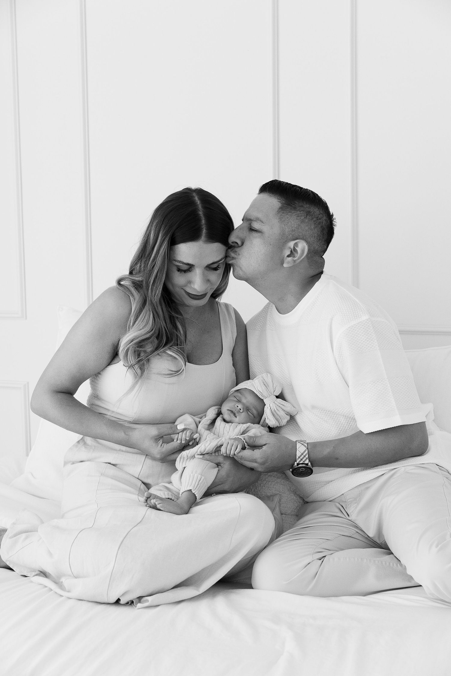 Intimate family photos on white bedding capturing tender moments with newborn.  Located in Palm Desert, California.