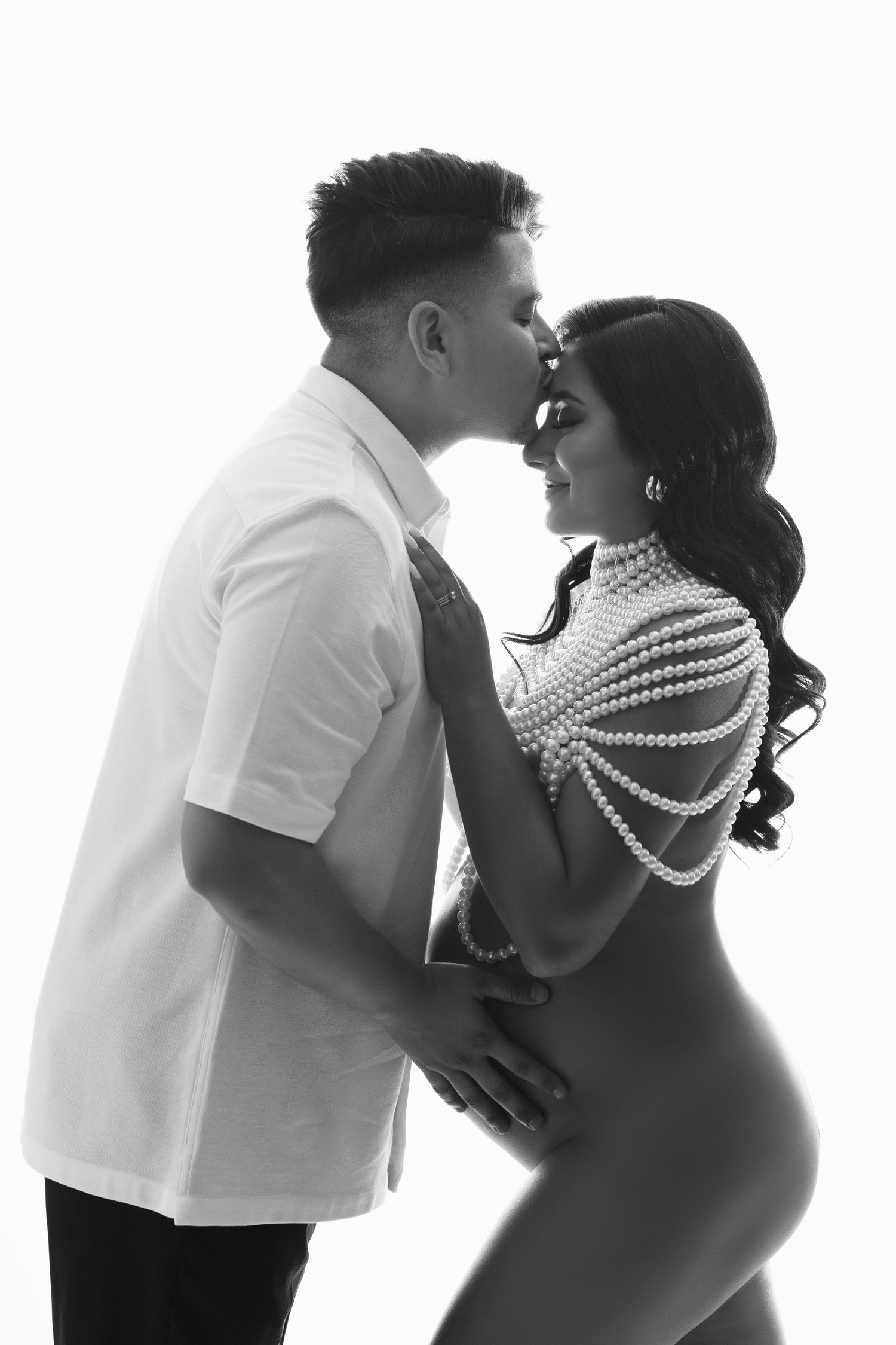 A romantic silhouette maternity photo series showing a couple embracing in white attire against a light background.