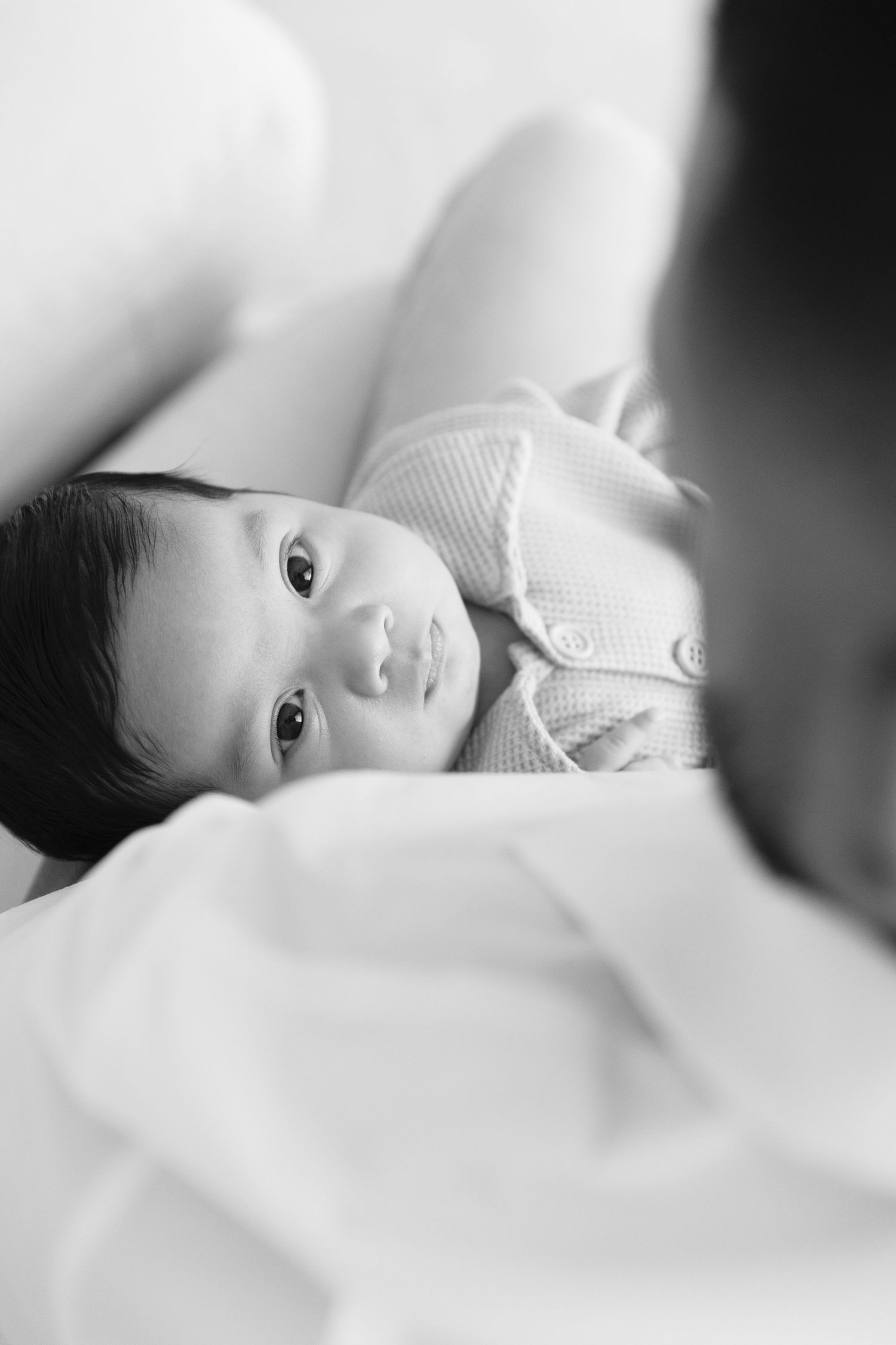 A black and white artistic portrait series of a baby lying on white bedding in soft focus.