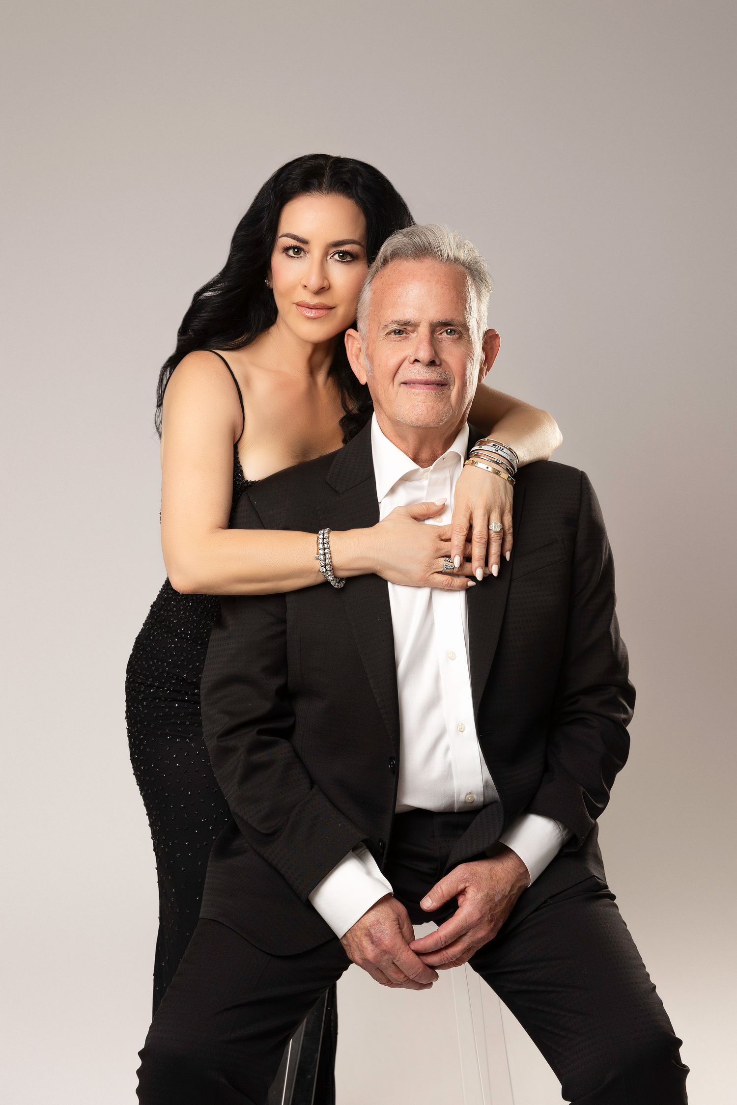 A couple poses together in formal attire against a light backdrop in a series of romantic studio portraits.