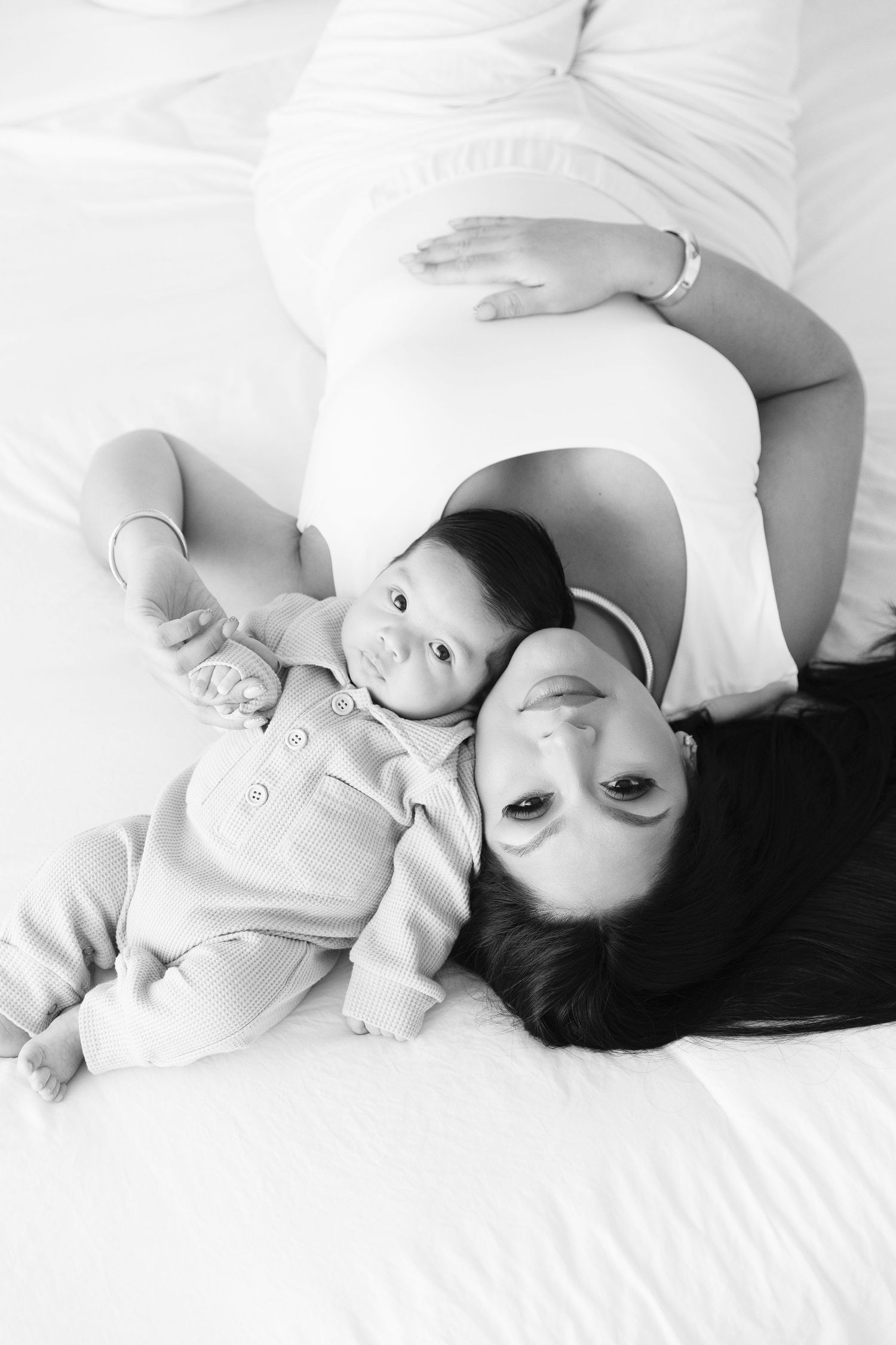 A tender black and white portrait of a parent and baby lying together on white bedding.  Newborn session Located in Palm Desert, California.