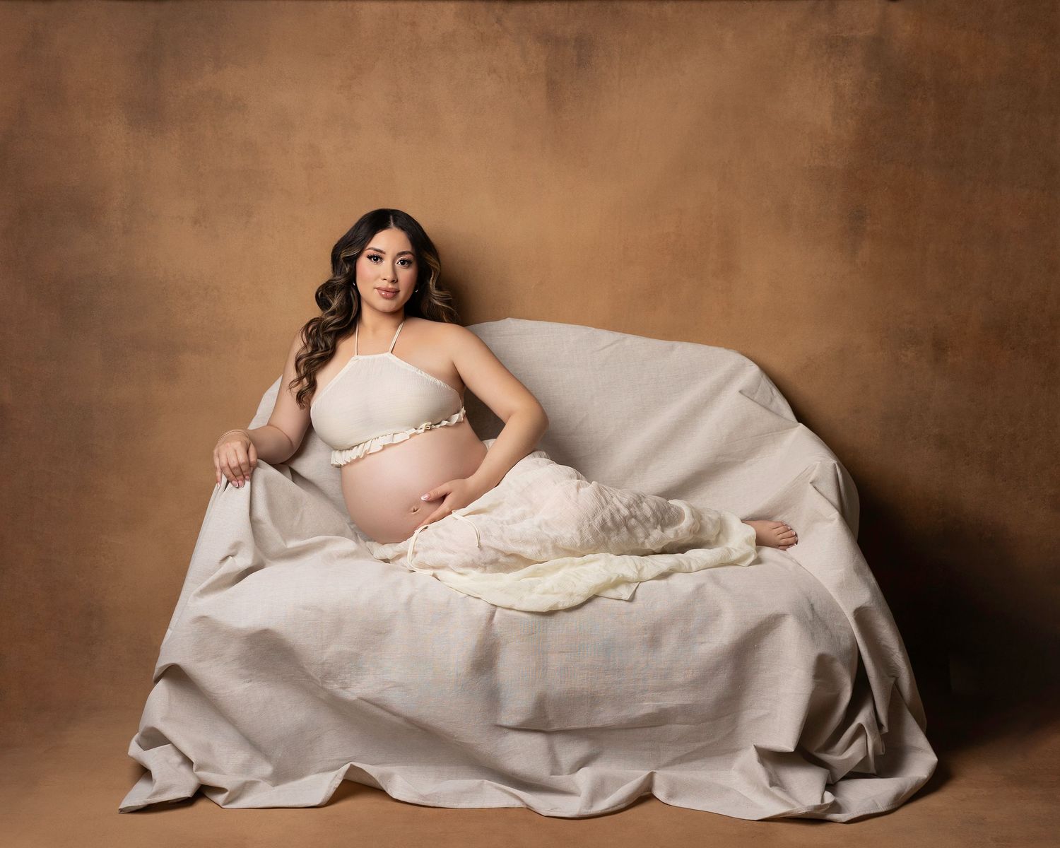 Maternity photography with soft brown backdrop and elegant draping fabric creating romantic atmosphere.  Located in Palm Desert, California.