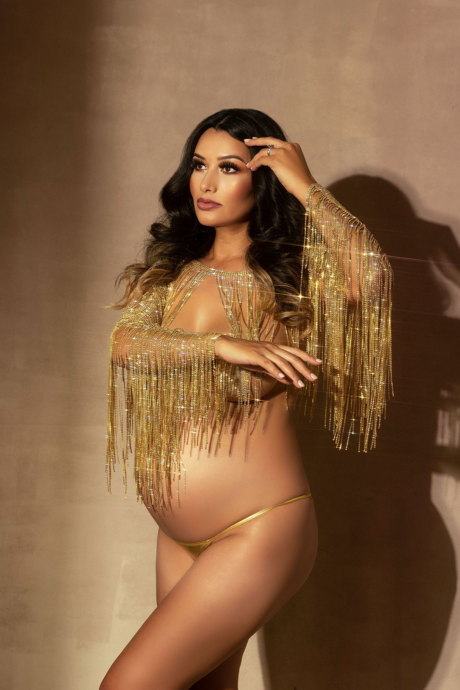 A maternity photoshoot featuring gold fringe details and dramatic lighting against a neutral backdrop.
