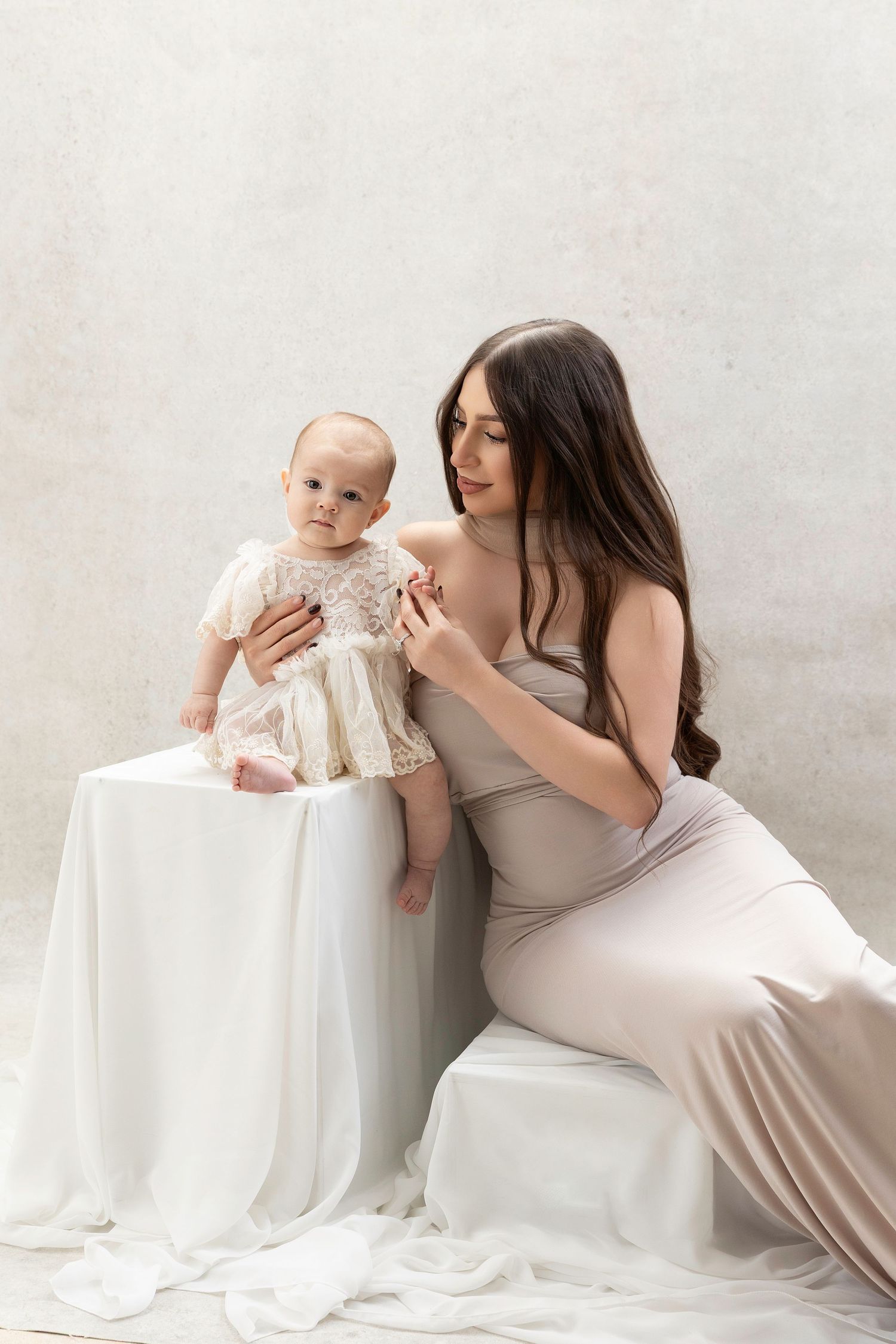 A tender moment captured in a minimalist studio setting with soft white fabric and neutral tones.