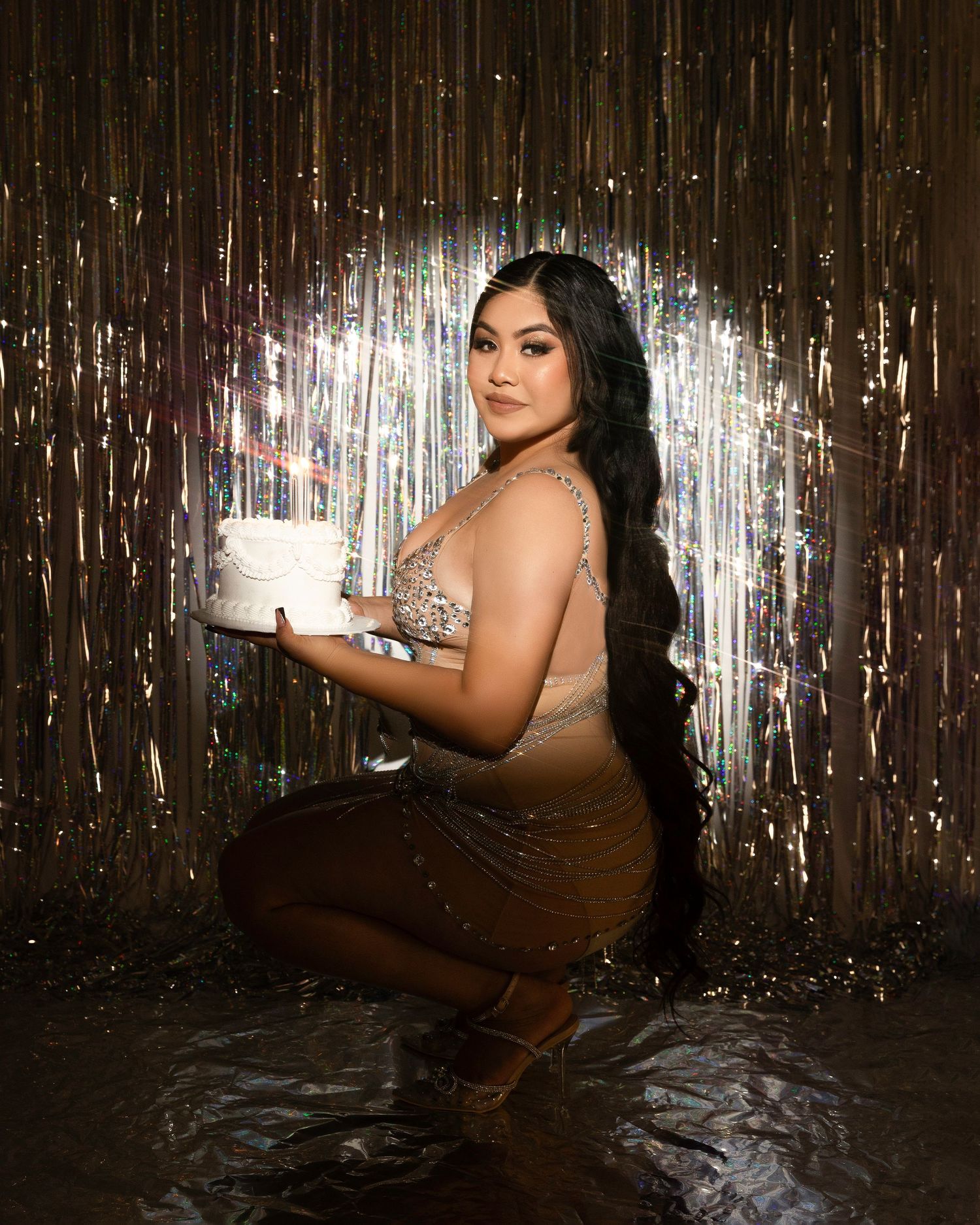 A glamorous photoshoot featuring a model posing against a metallic tinsel backdrop in dramatic lighting.