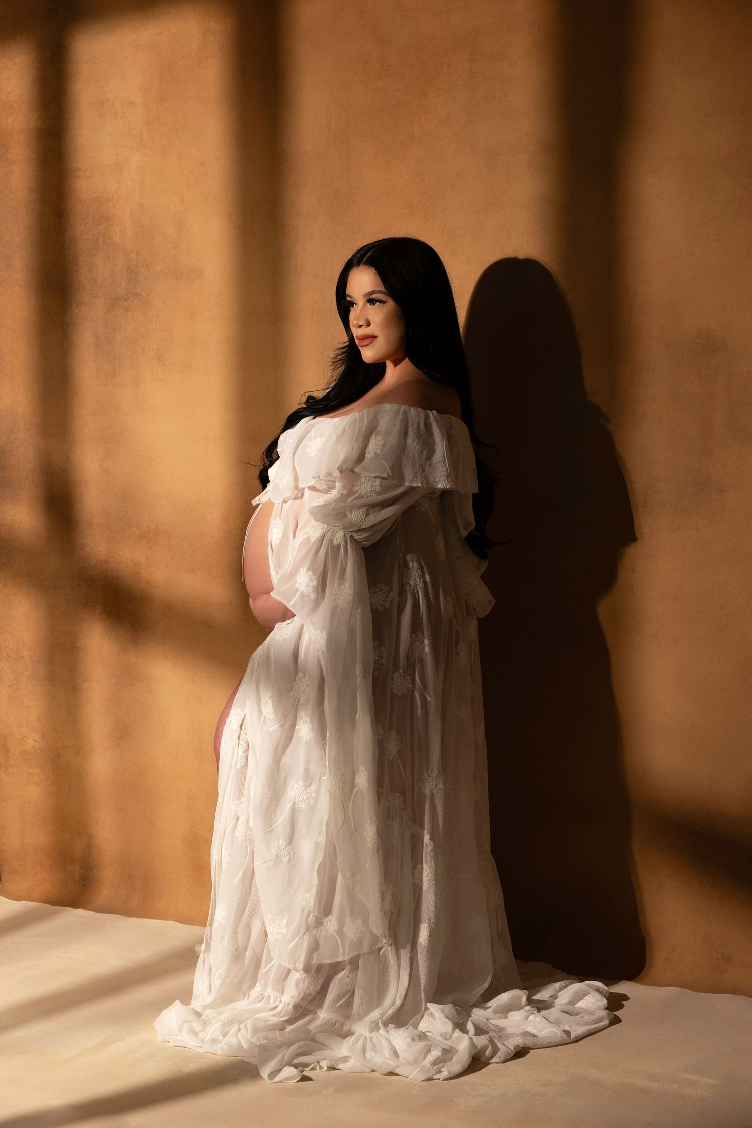 Ethereal maternity portraits in flowing white dress against warm brown backdrop.  Located in Palm Desert, California.