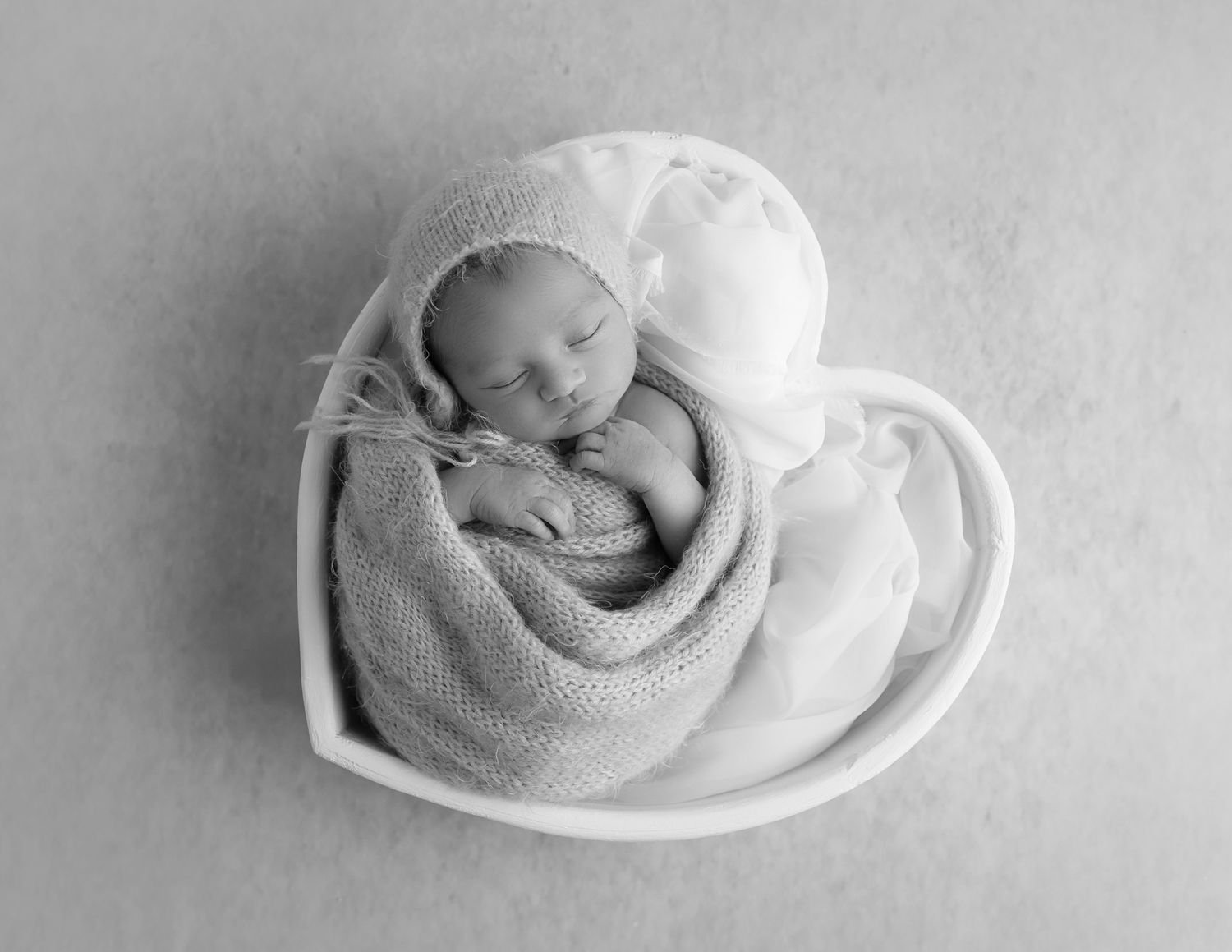 A series of black and white photographs showing a sleeping newborn baby curled up in white fabric.