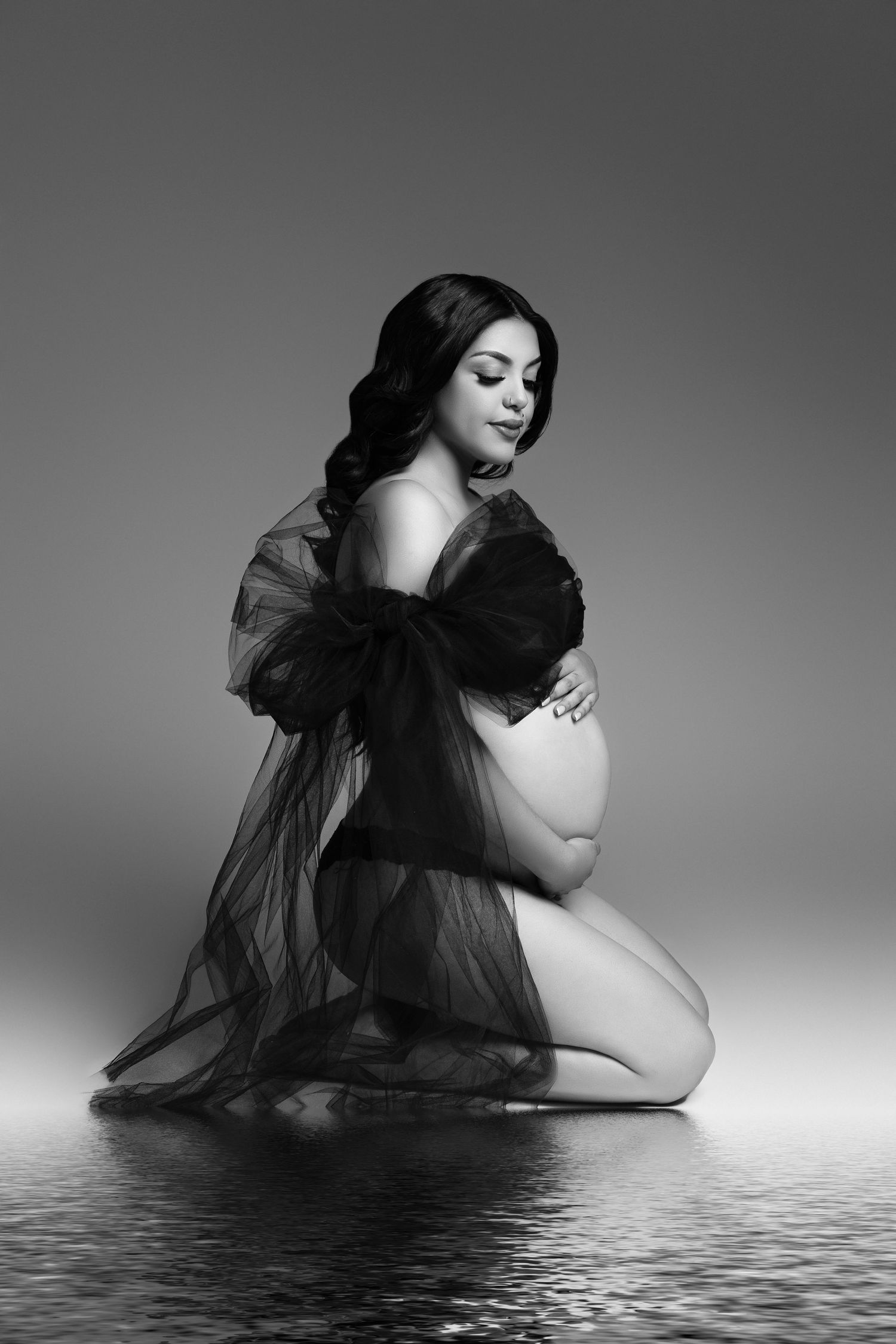 An artistic black and white maternity photo with a figure kneeling in sheer black tulle.  Located in Palm Desert, California.