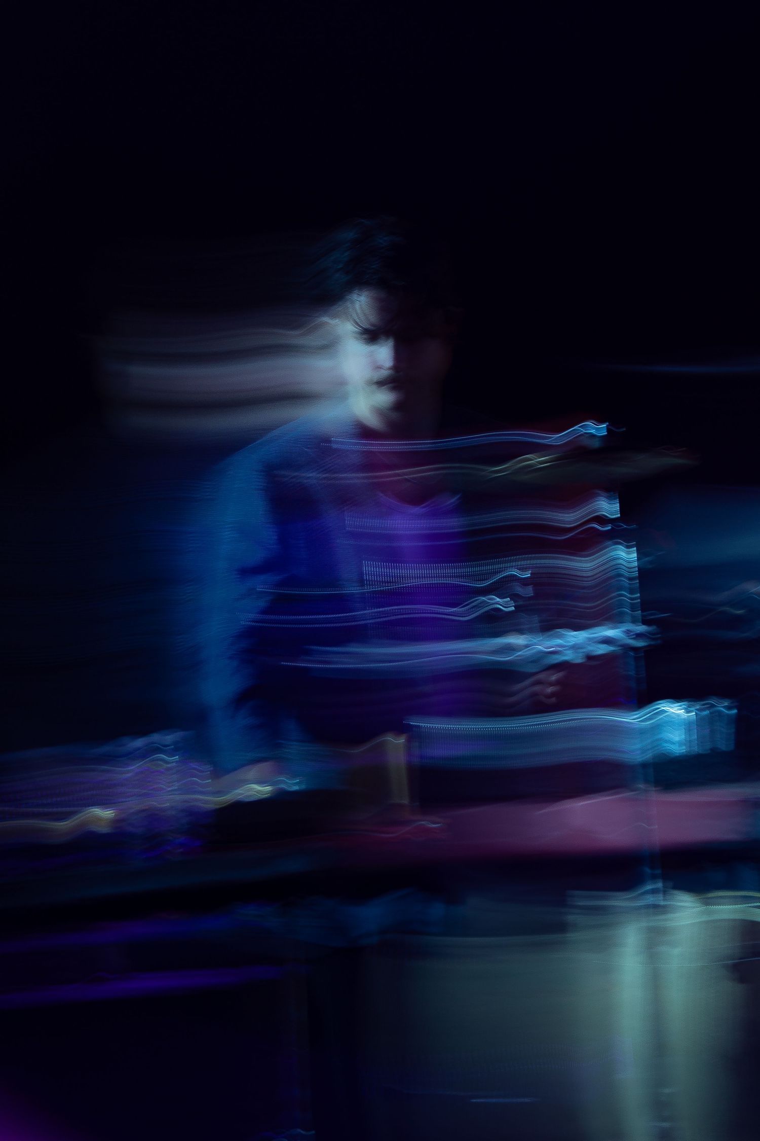 Abstract long exposure concert photo with colorful light trails surrounding a performer in blue lighting.
