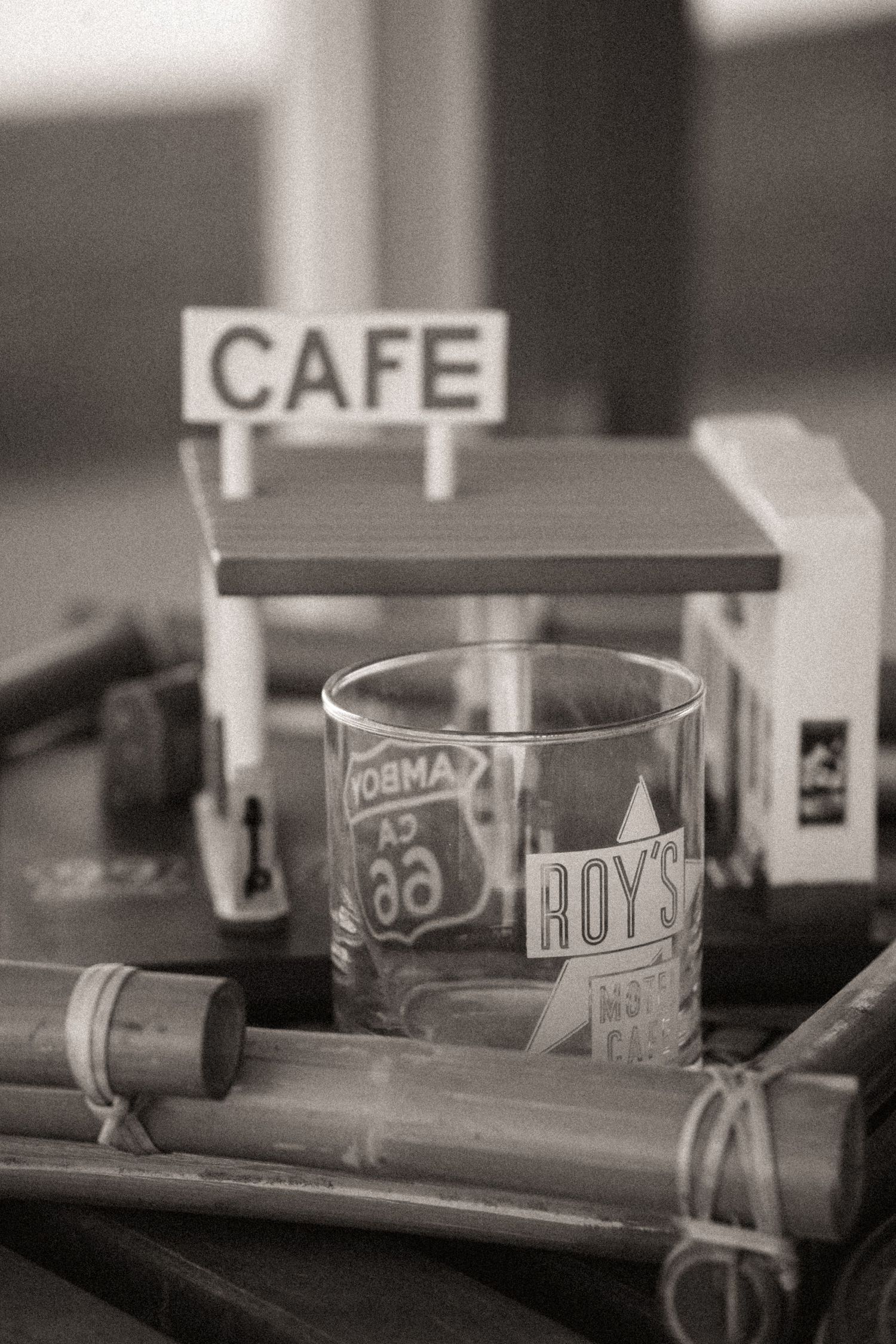 Black and white close-up of a Roy's Motel Cafe souvenir glass beside a miniature cafe sign.