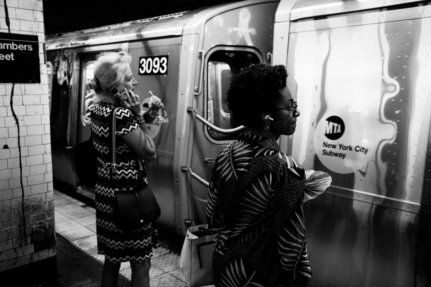 Black and white photo of two women in patterned dresses waiting at a New York City subway platform.