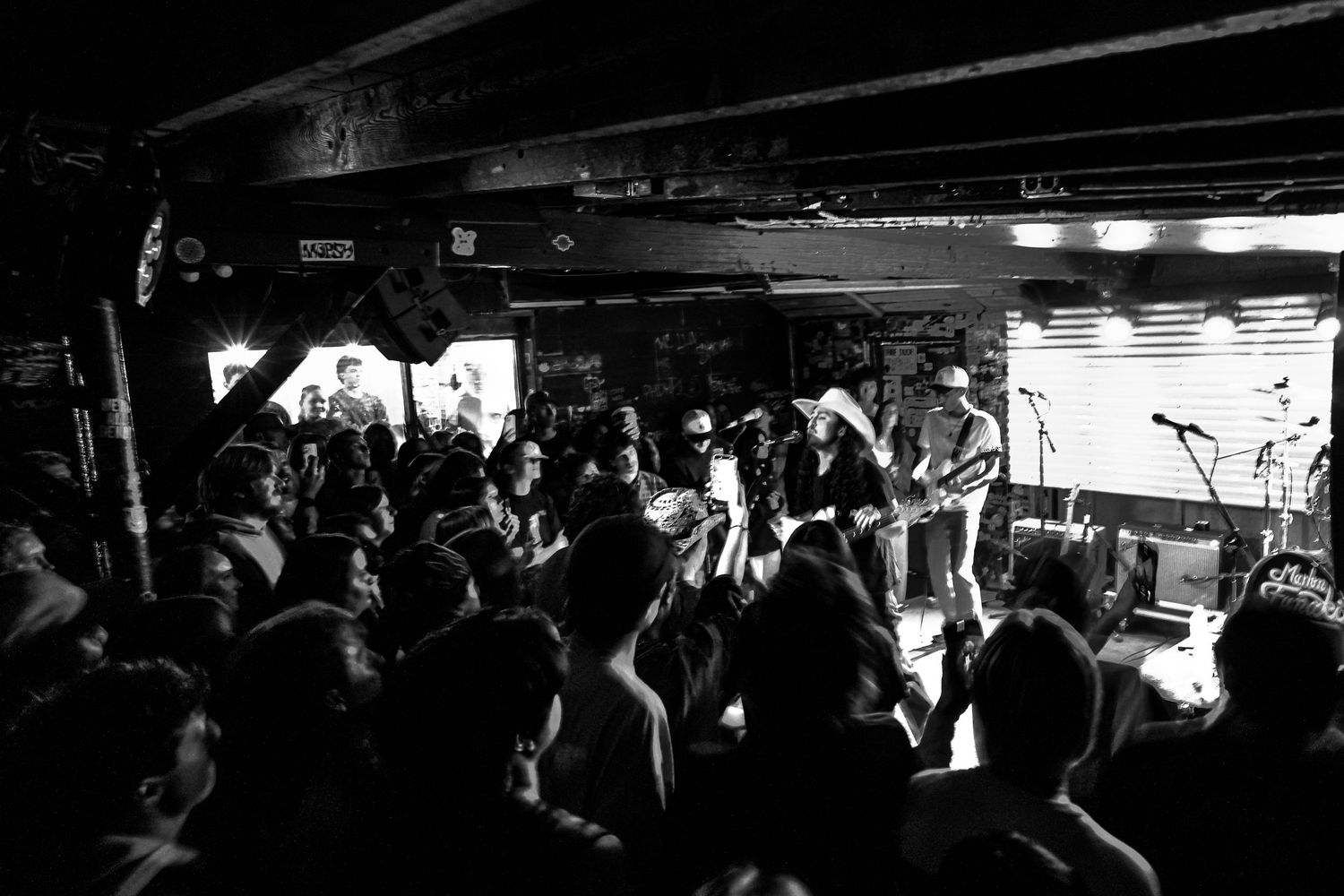 Black and white wide shot of packed music venue crowd watching live band performance on stage.