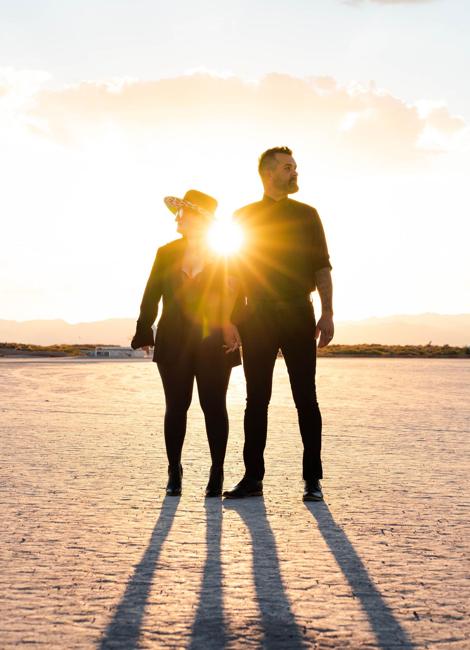 Couple silhouetted against a stunning golden sunset on a vast flat desert landscape.