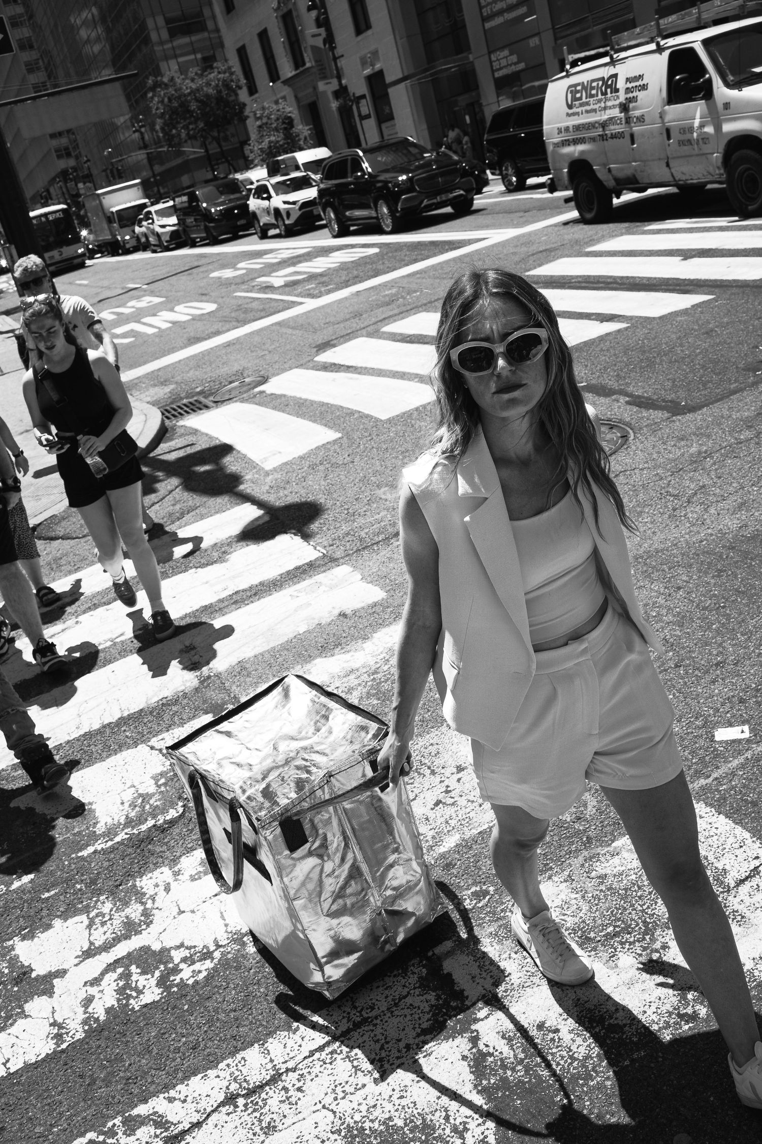 Black and white photo of a woman in white suit crossing a city street.