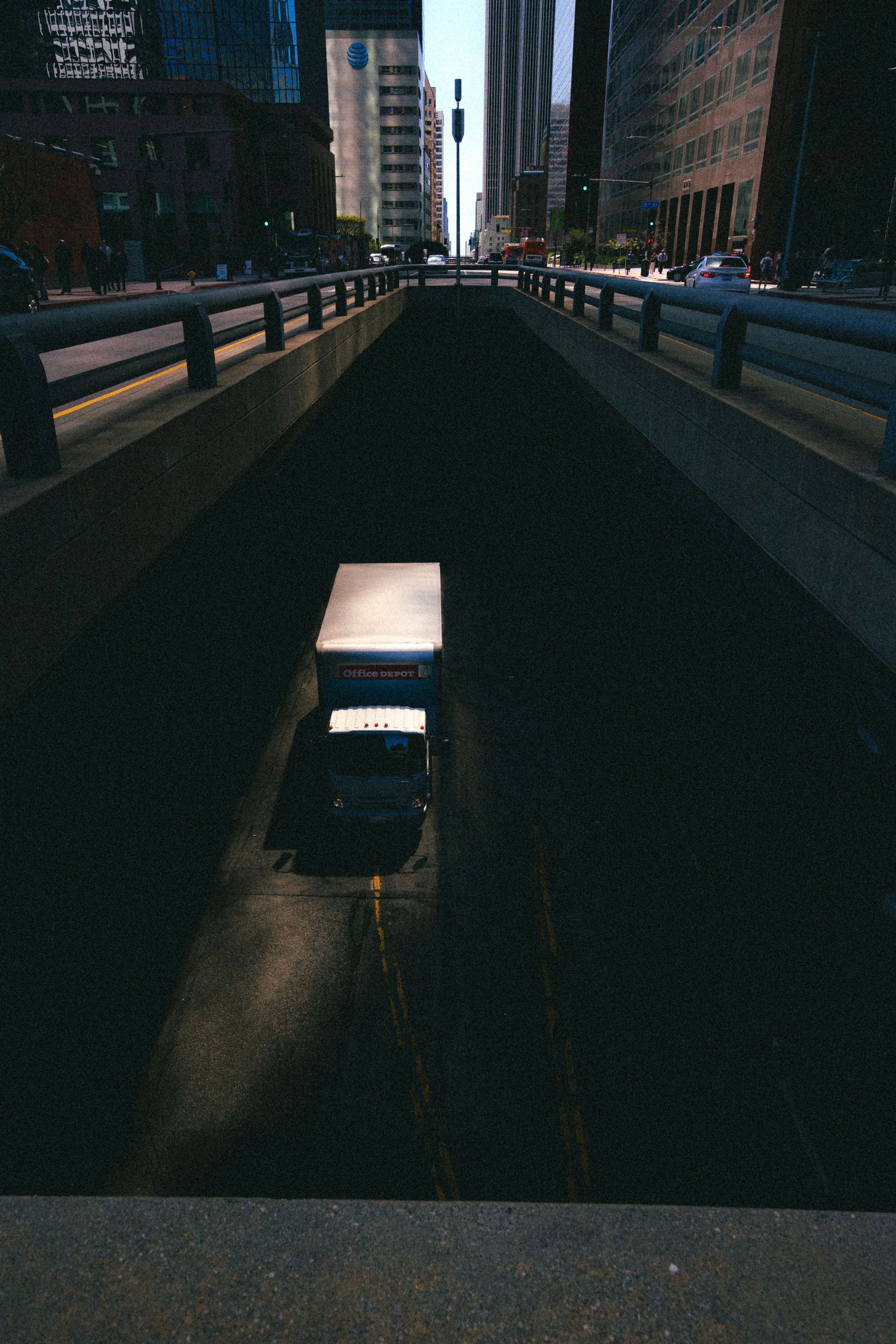 A delivery truck emerges from a dark urban underpass surrounded by city skyscrapers in black and white.