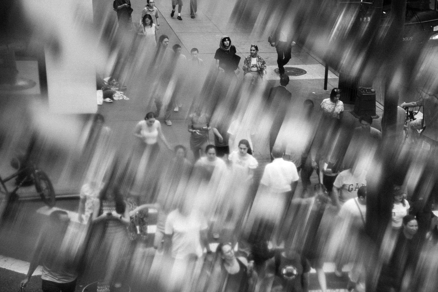 Black and white motion blur aerial photo of crowds of people walking in a public space.