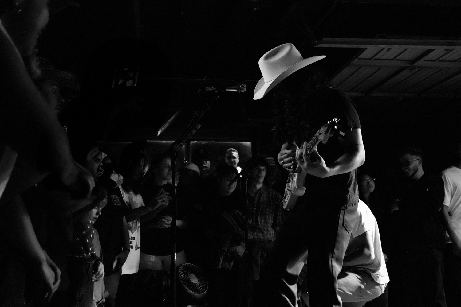 Black and white photo of concert crowd with performer in cowboy hat and photographer capturing the show.