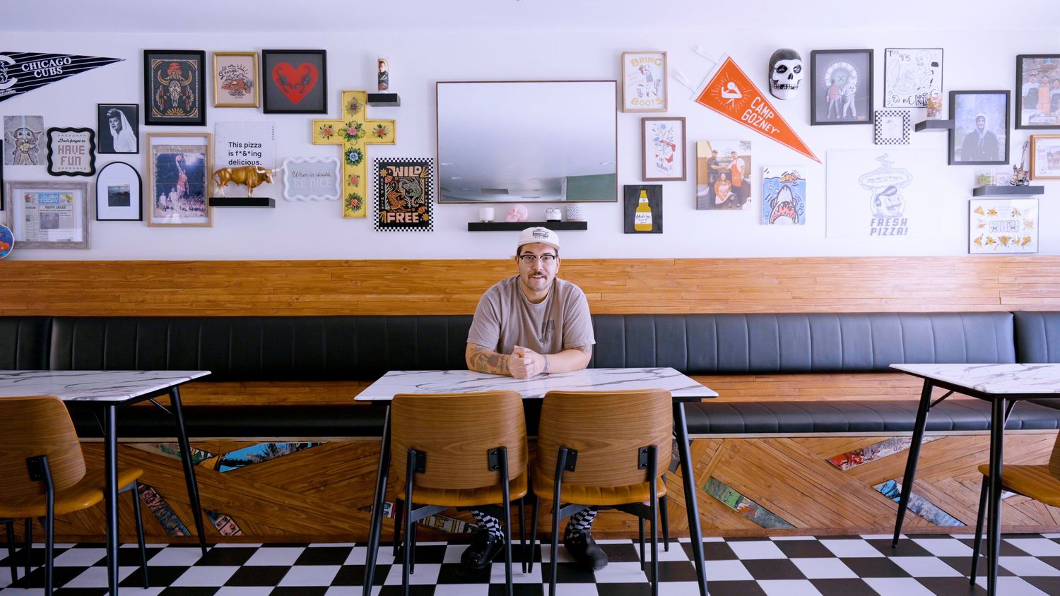 Man sitting alone at a school desk in a retro diner with eclectic wall art decor.