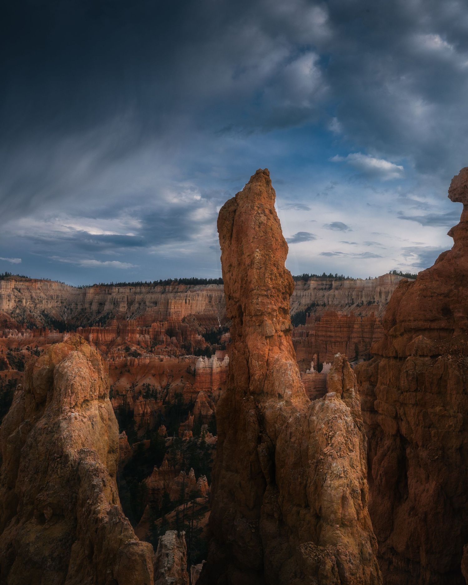 A towering red rock hoodoo spire rises dramatically above Bryce Canyon under a moody stormy sky.