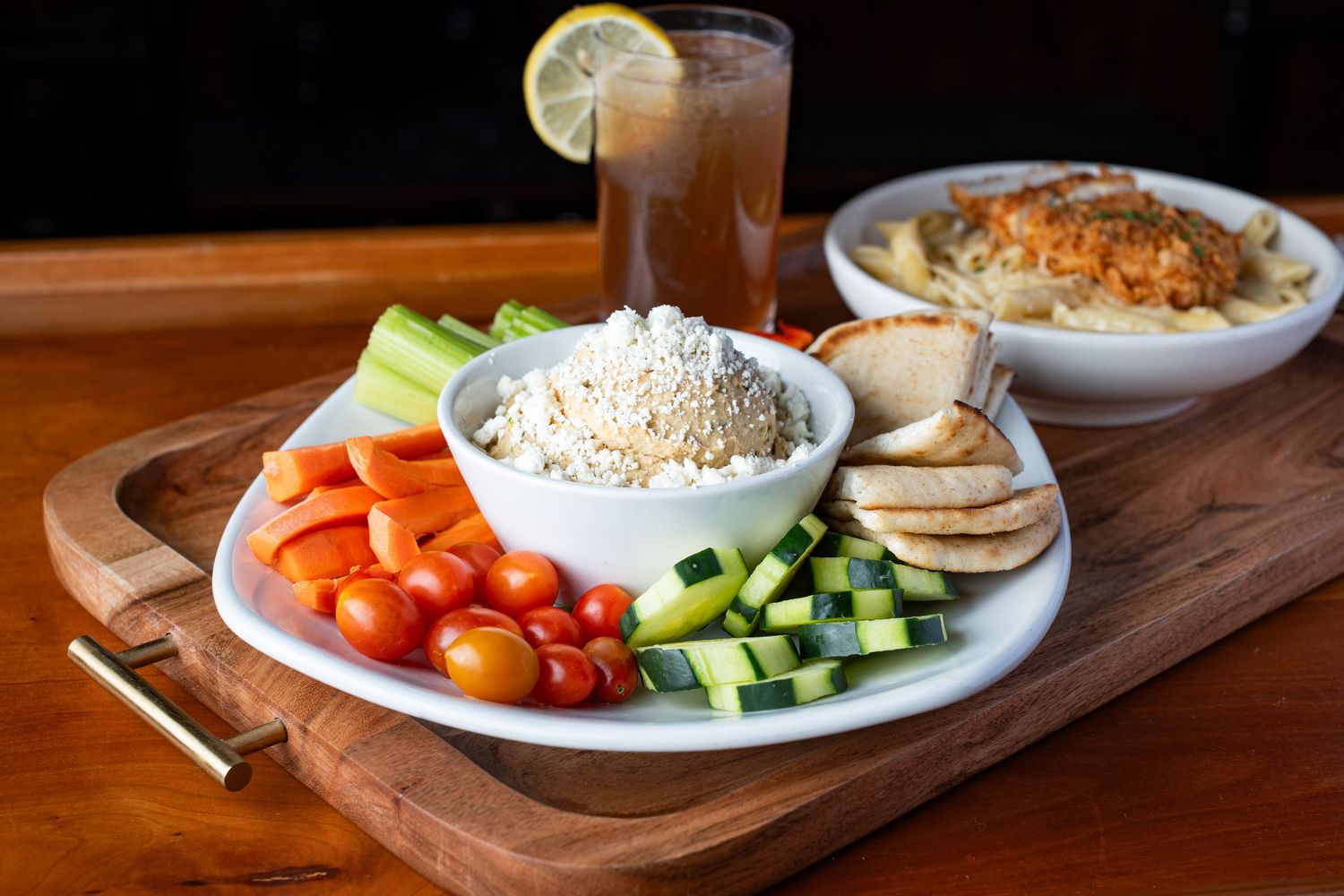 Fresh vegetable and hummus platter with pita, cherry tomatoes, and cucumbers served with an iced tea.