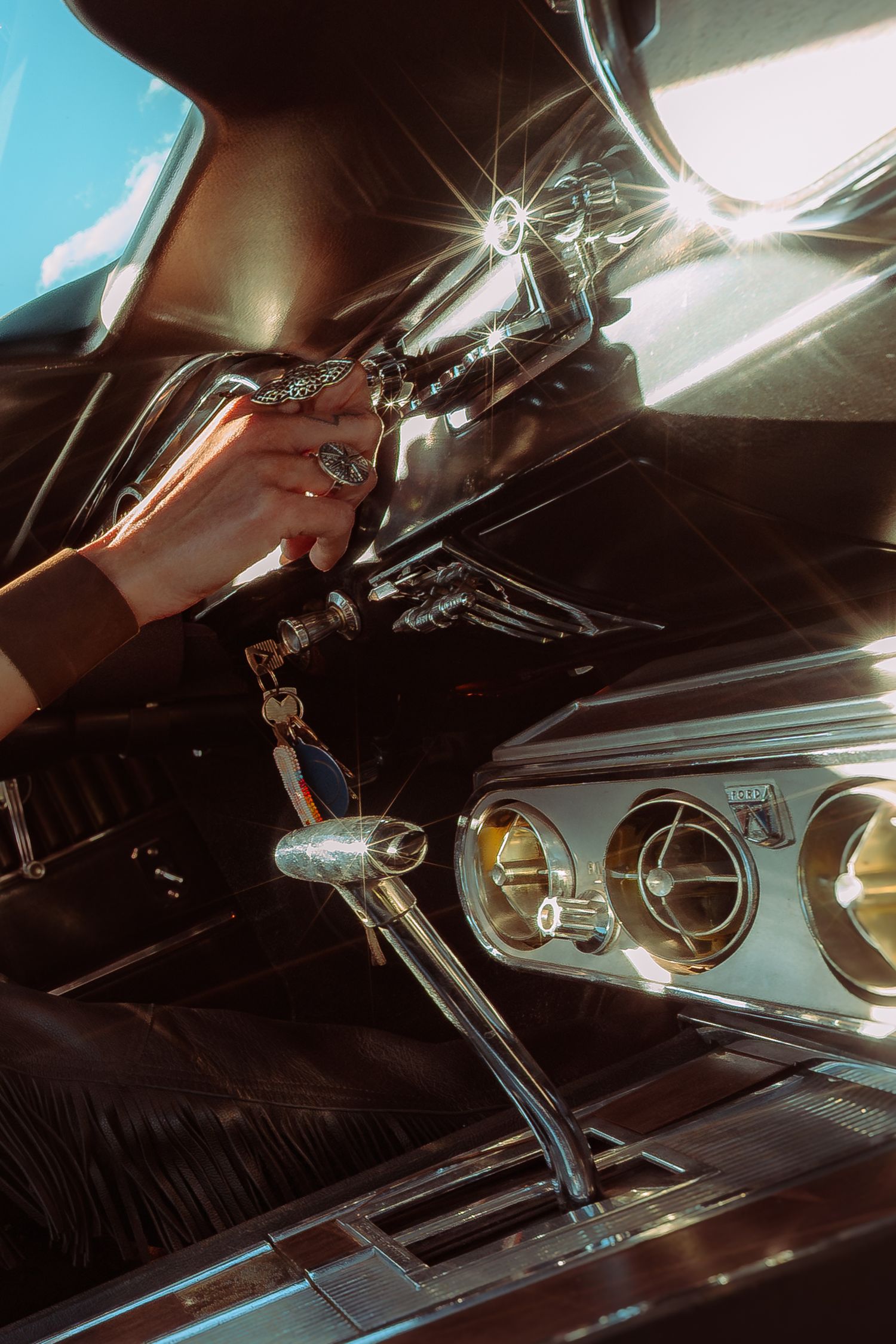 Close-up of a hand with rings adjusting a vintage car's chrome gear shift inside a classic vehicle interior.