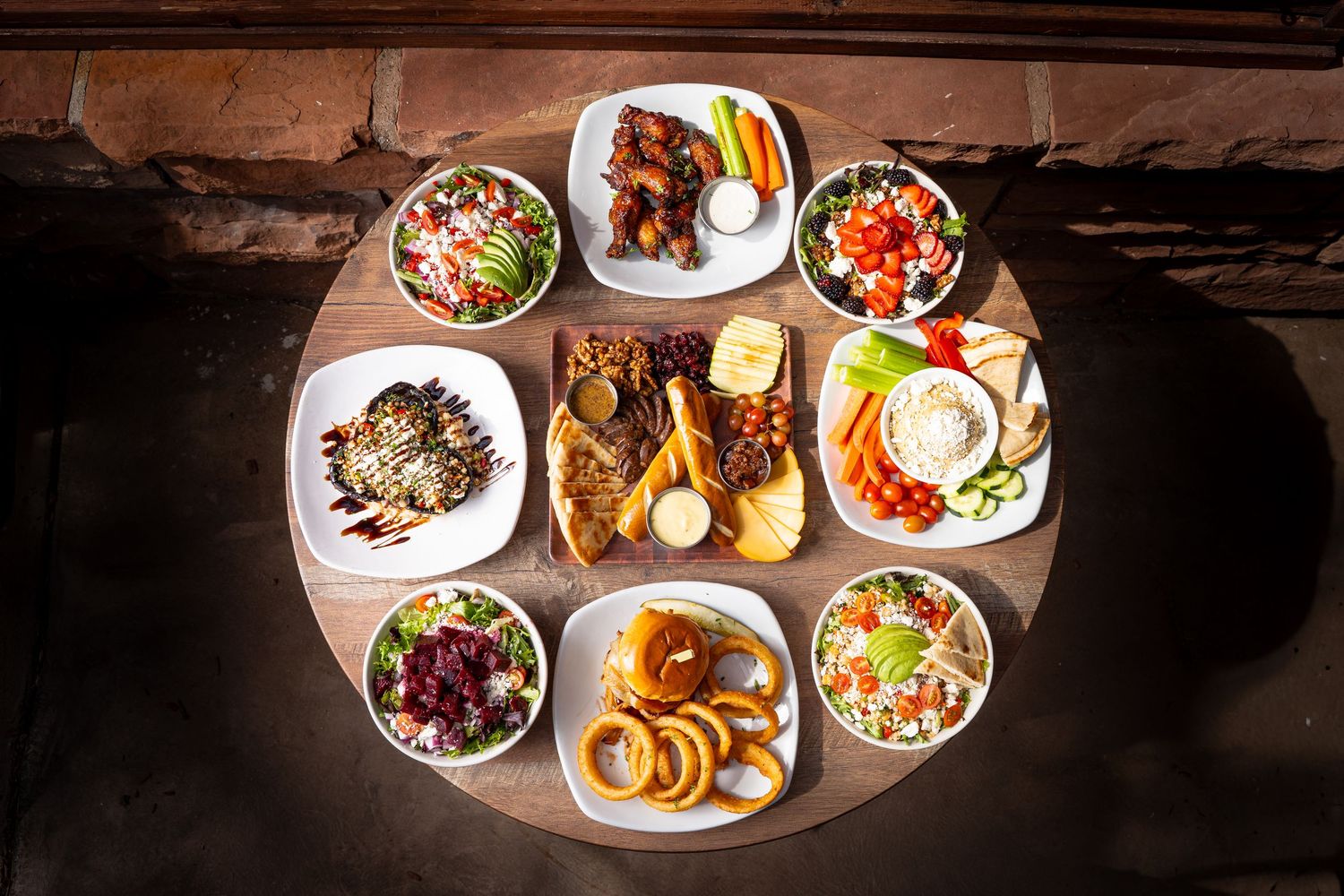 Overhead view of assorted appetizers and salads arranged on a round wooden table in a restaurant.