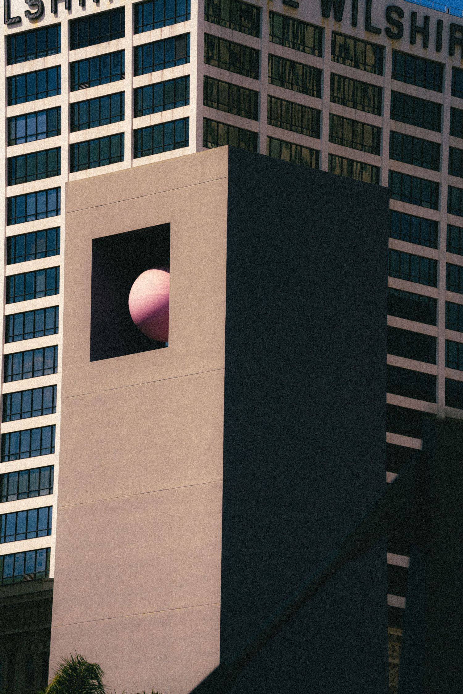 Pink sphere sculpture in a square opening on a modern building facade.