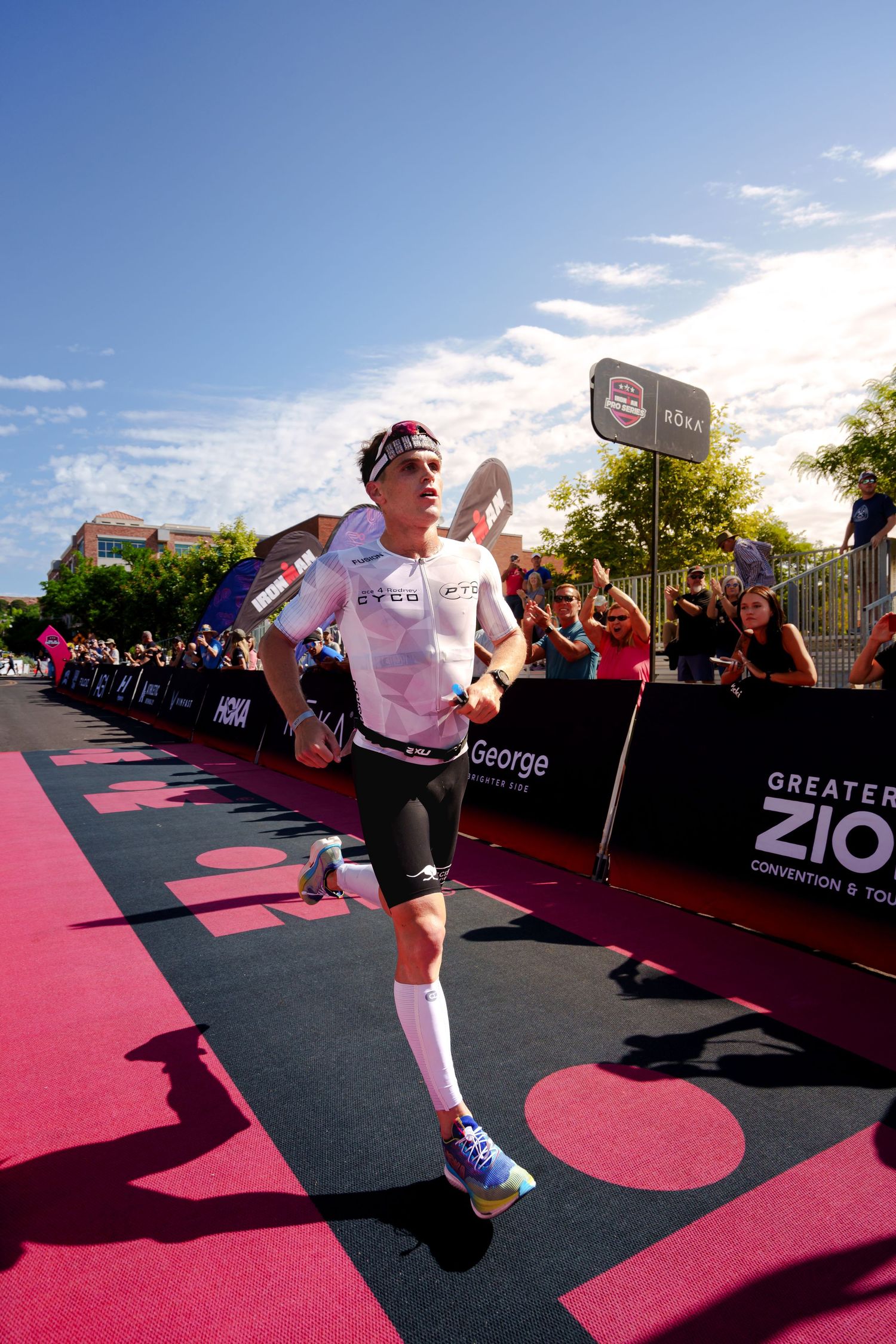 A triathlete runs through the finish chute at the Greater Zion Ironman event cheered on by spectators.