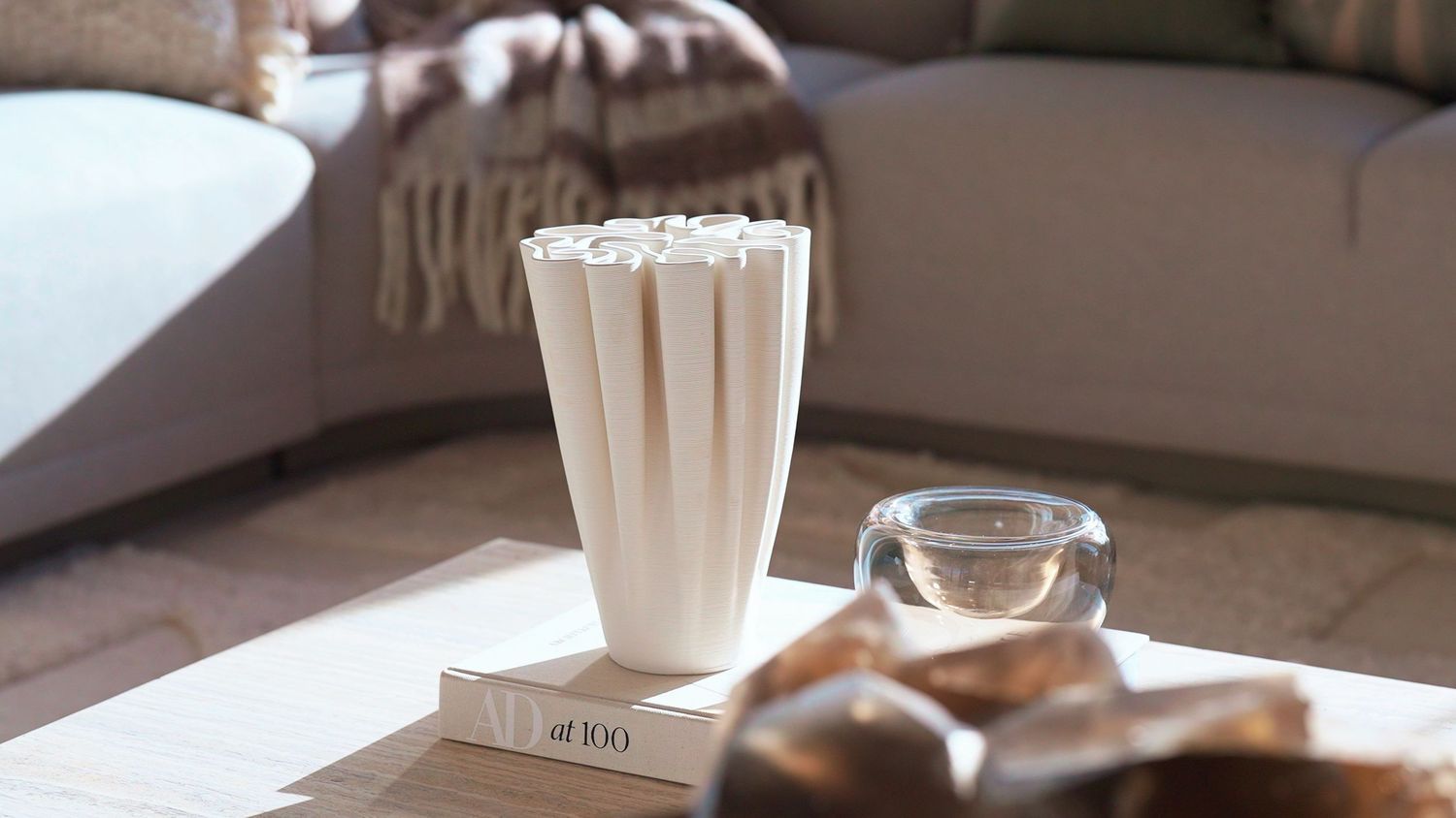 White decorative vase on coffee table with glass bowl in sunlight.