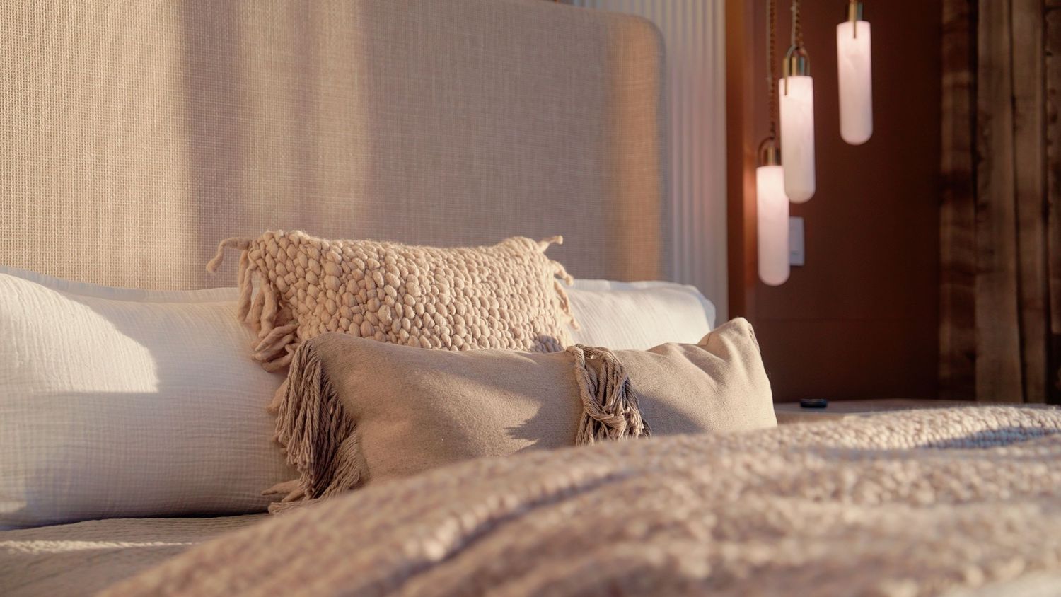 Elegant bed with layered pillows and pendant lights in warm tones.