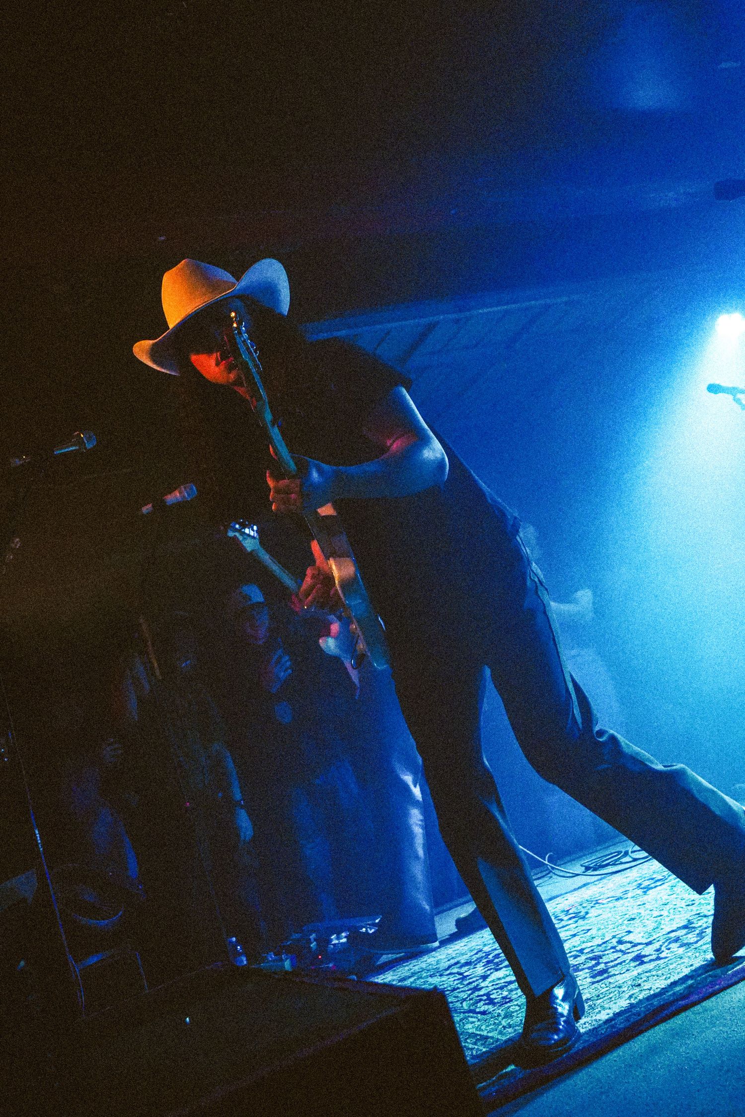 Live concert performer in cowboy hat playing guitar under dramatic blue stage lighting.