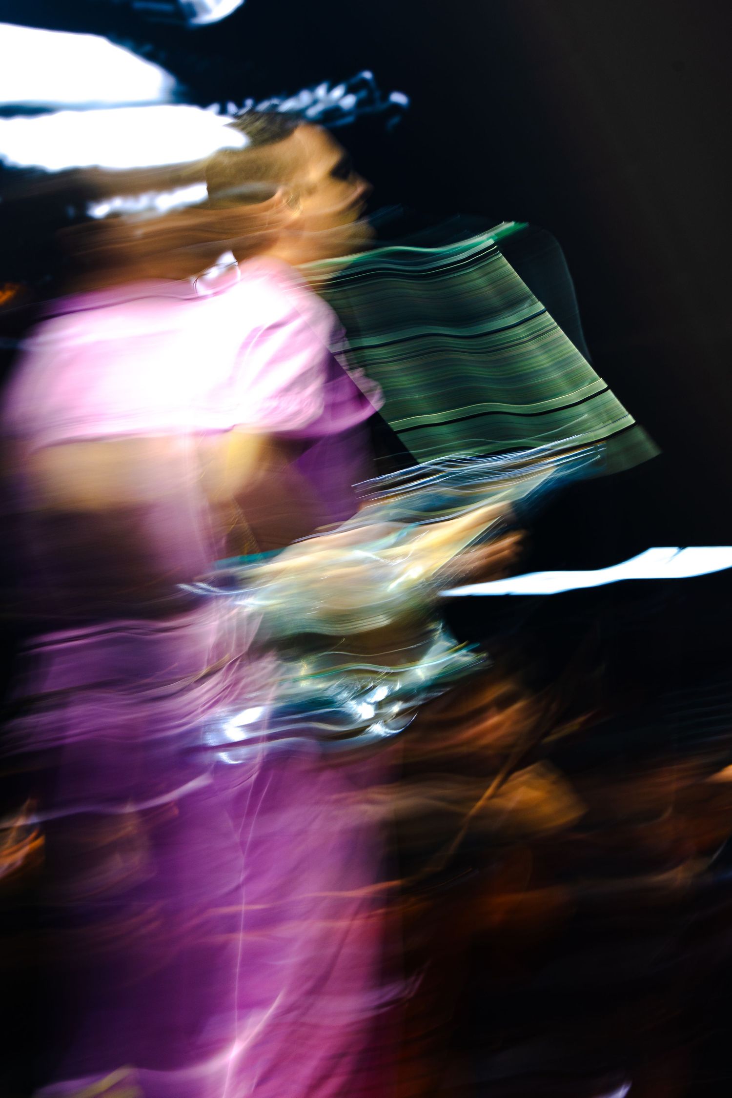 Abstract motion blur of a performer in purple holding a striped cloth under dark stage lighting.